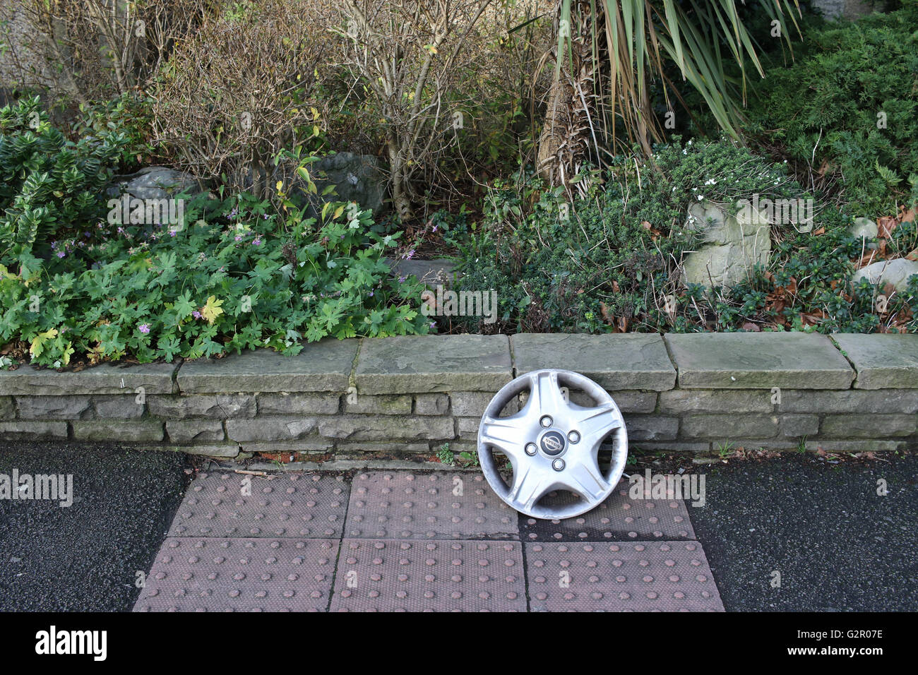 Discarded car wheel trim against low stone wall, bushes Stock Photo