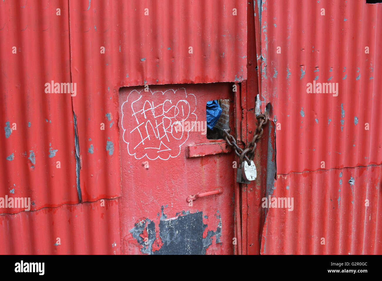 red corrugated metal door, gate with graffiti, wear, padlock, rusty chain Stock Photo