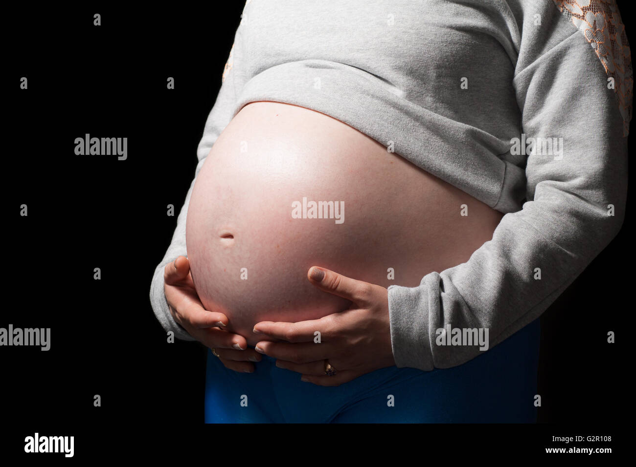 Close-up holding pregnant stomach, black isolated background. Stock Photo