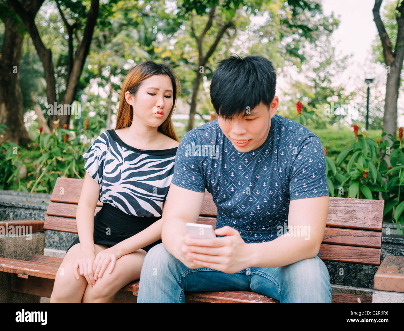 Jealous girlfriend peeking and spying her boyfriend mobile phone while he is reading a message Stock Photo