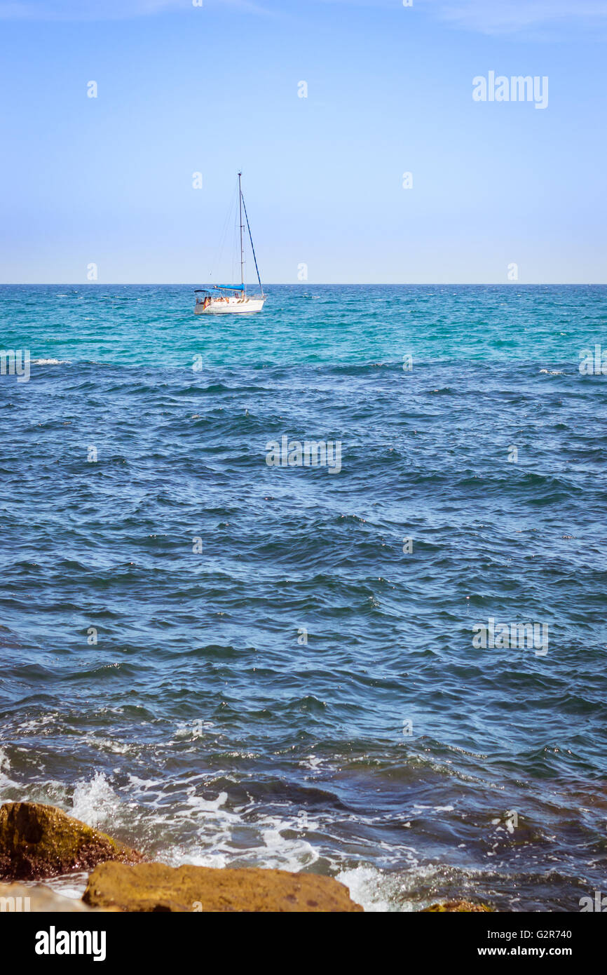 Sailboat floating in sea on horizon, coast of Sunny beach, Av de los Marineros, Torrevieja, Valencian Community, Spain Stock Photo
