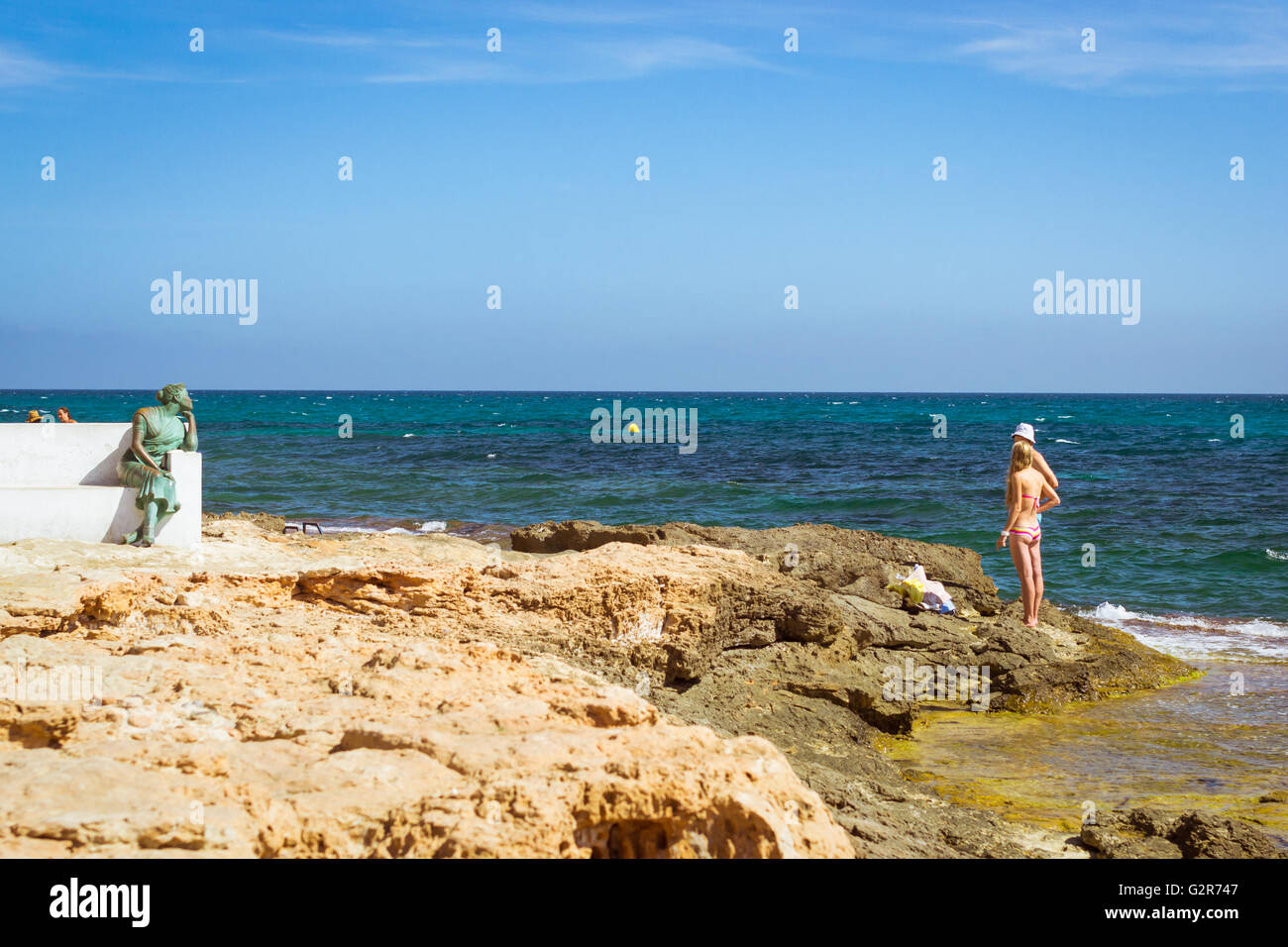 TORREVIEJA, SPAIN - SEPTEMBER 13, 2014: Bronze monument to sailor's wife, Sunny Mediterranean beach, Tourists relax in water Stock Photo