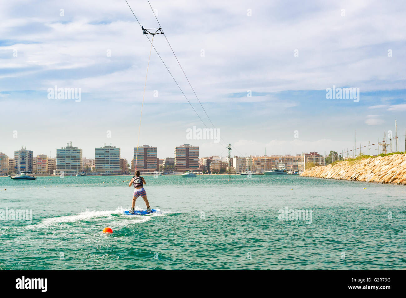 TORREVIEJA, SPAIN - SEPTEMBER 13, 2014: Cute girl learns to surf on background of yachts and boats in La Bocana, Cable Ski Stock Photo