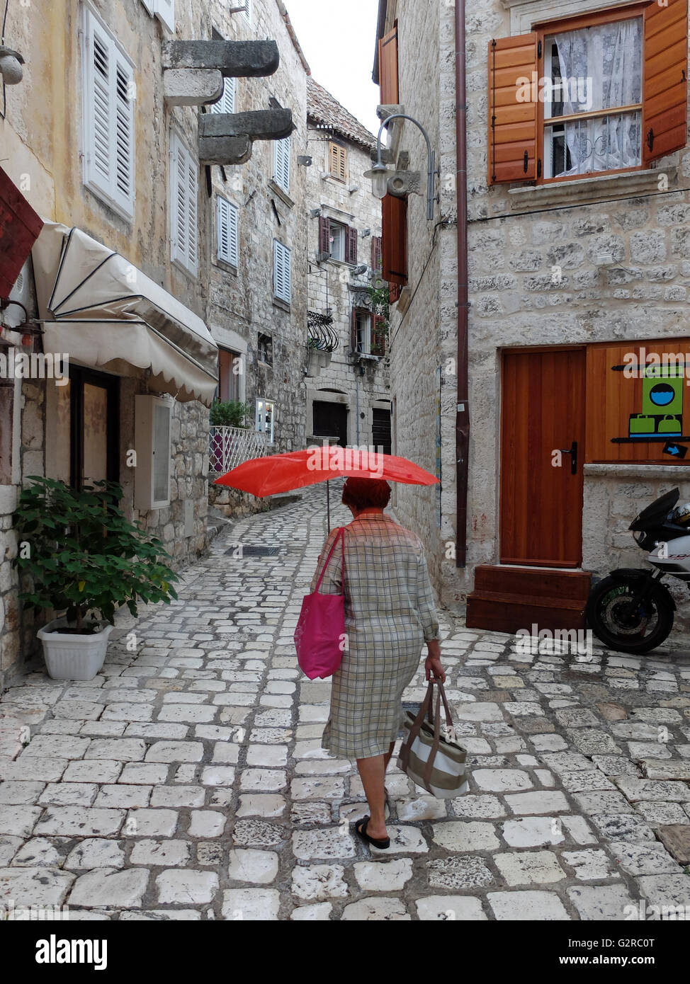 19.08.2015, Hvar, Split-Dalmatia, Croatia - Woman with red umbrella going through the streets. 0BG150819D063CAROEX.JPG - NOT for SALE in G E R M A N Y, A U S T R I A, S W I T Z E R L A N D [MODEL RELEASE: NO, PROPERTY RELEASE: NO, (c) caro photo agency / Geilert, http://www.caro-images.com, info@carofoto.pl - Any use of this picture is subject to royalty!] Stock Photo