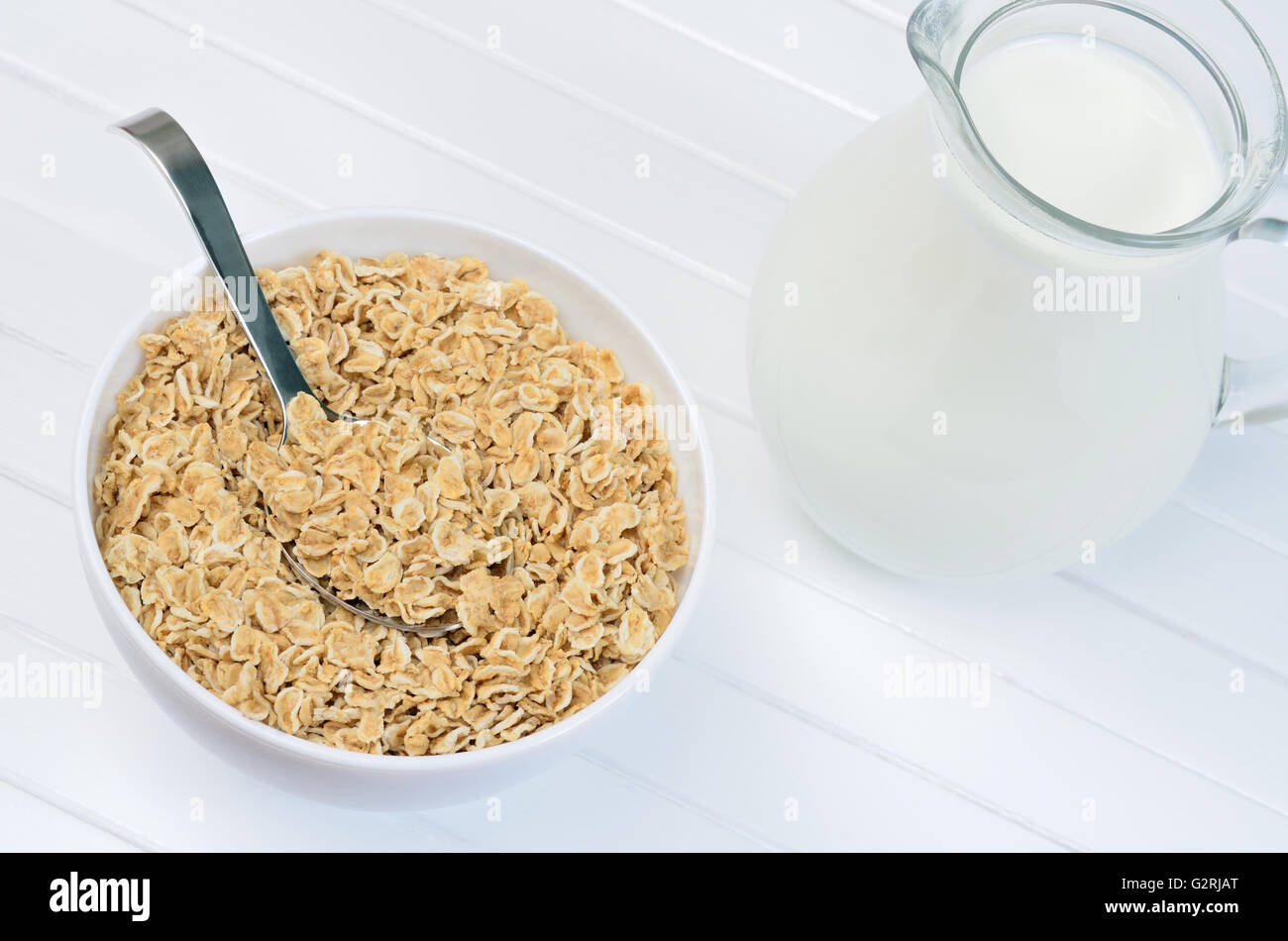 Healthy oatmeal in a white bowl and pitcher with milk on wooden table Stock Photo