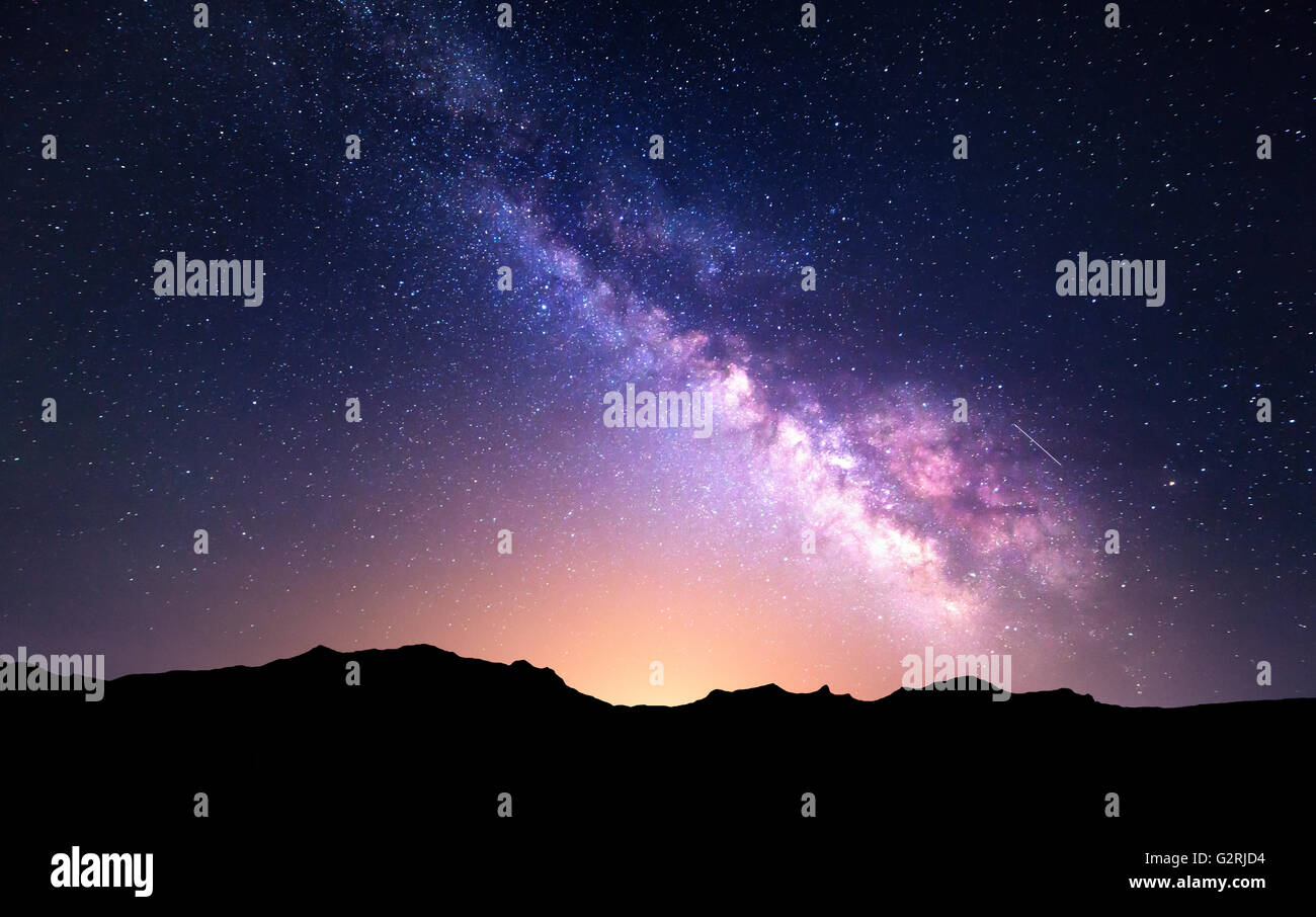 Night landscape with colorful Milky Way and yellow light at mountains. Starry sky with rocks at summer. Beautiful Universe Stock Photo