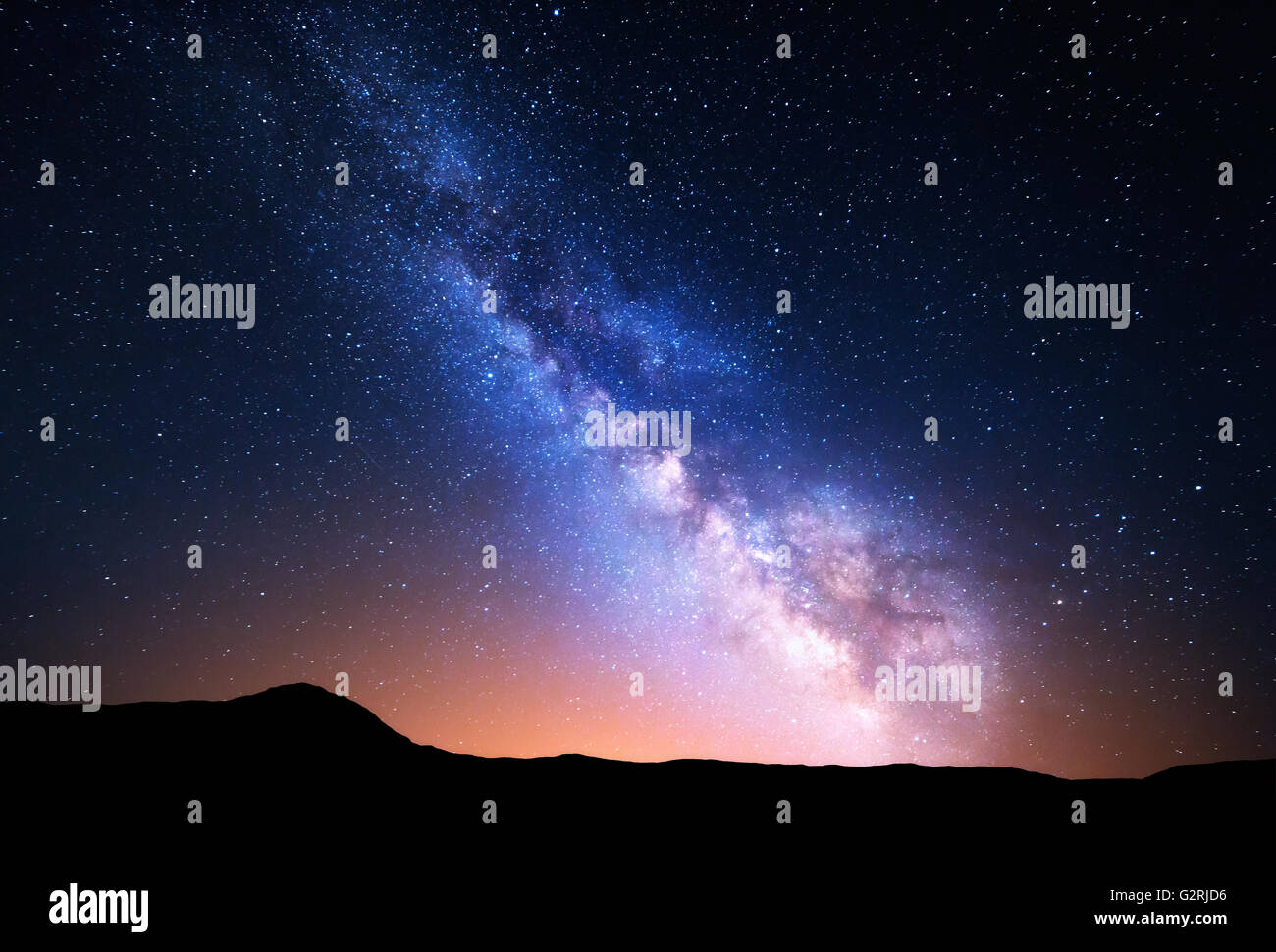 Night landscape with colorful Milky Way and yellow light at mountains. Starry sky with rocks at summer. Beautiful Universe Stock Photo