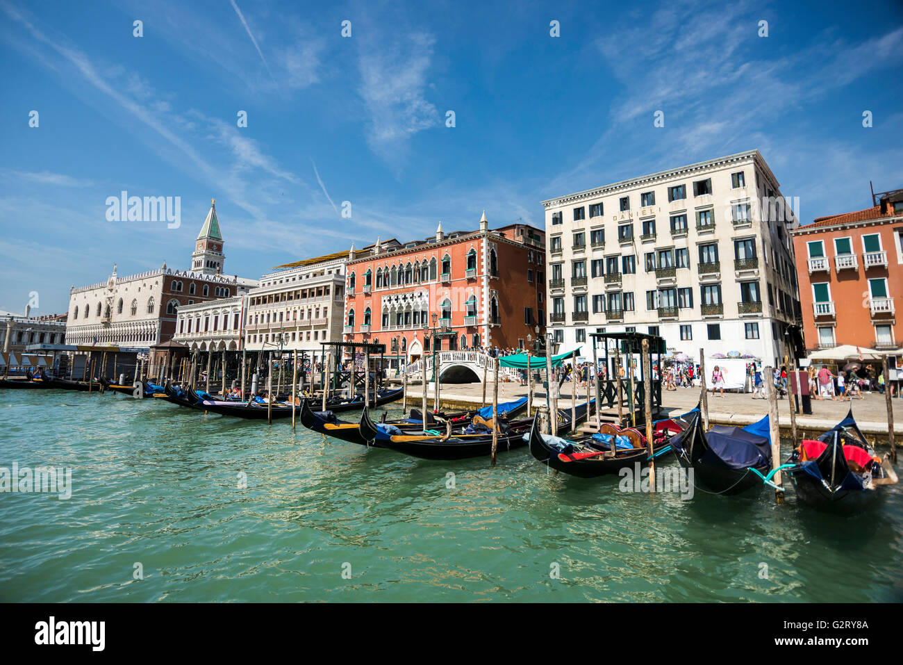 Gondolas attached to the main Venice road with people walking behind on