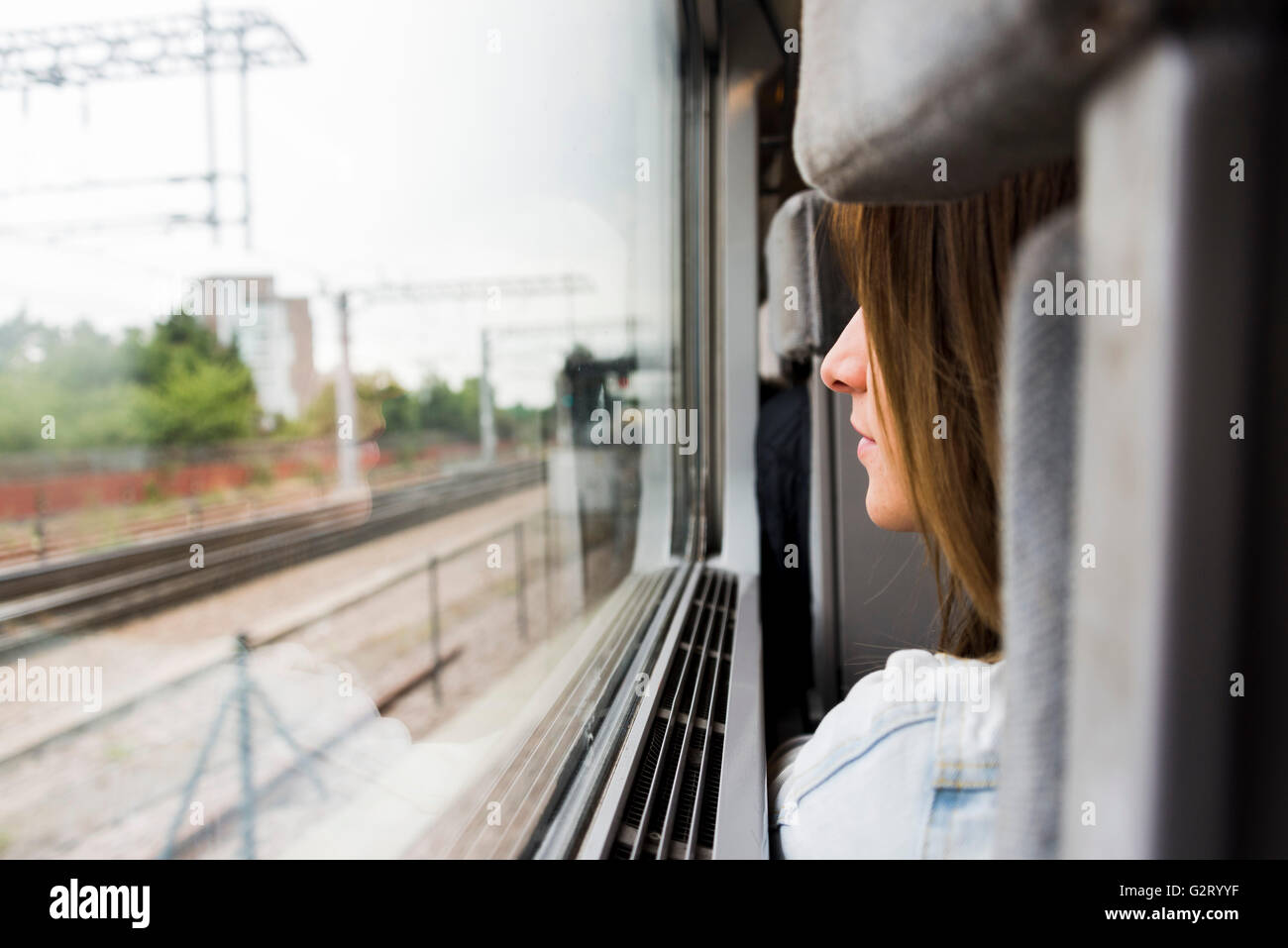 A young woman sitting on a train seat looking throught the window at the city passing by. Stock Photo