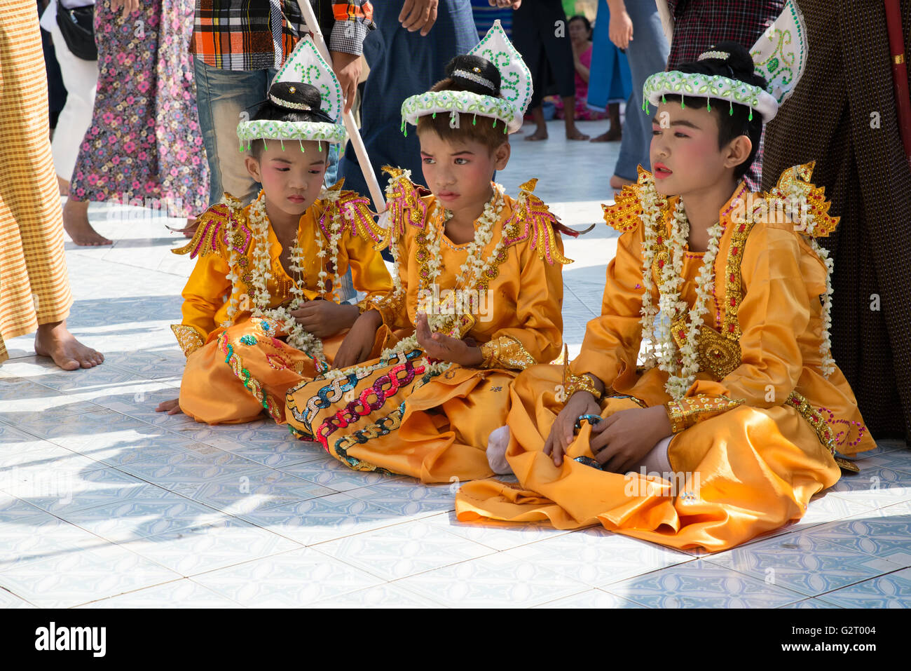 Three boys dressed for shinbyu novitiation ceremony sitting on the ground, Botataung Pagoda, Yangon, Yangon State, Myanmar Stock Photo