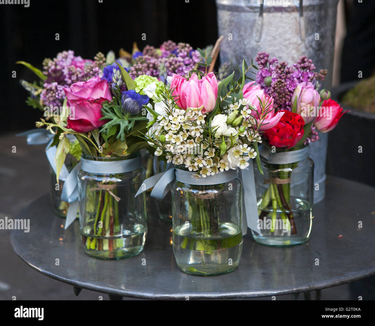 Small bouquets of lilacs, hyacinths, anemones, roses and peonies in small glass jars on an iron table. Stock Photo