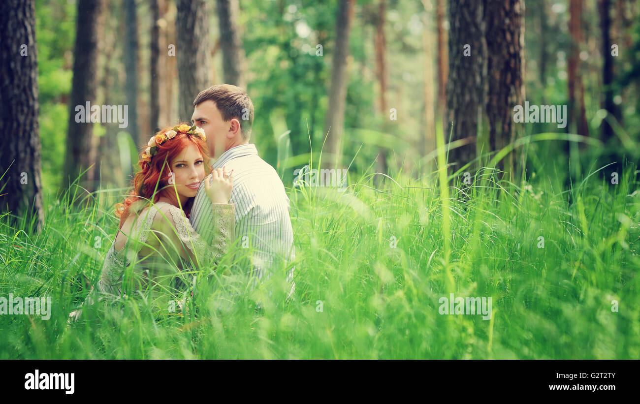 Portrait of a young gentle couple sitting on a fresh green grass in the forest, hugging and enjoying spending time together Stock Photo