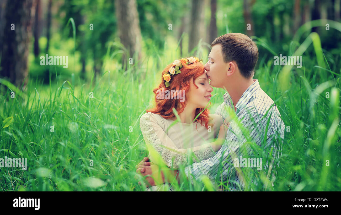 Portrait of a young gentle couple sitting on a fresh green grass in the ...