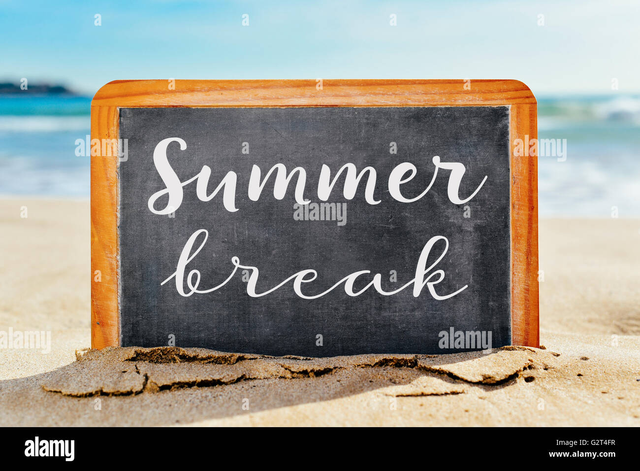 closeup of a chalkboard with a wooden frame and the text summer break written in it, placed on the sand of a beach Stock Photo