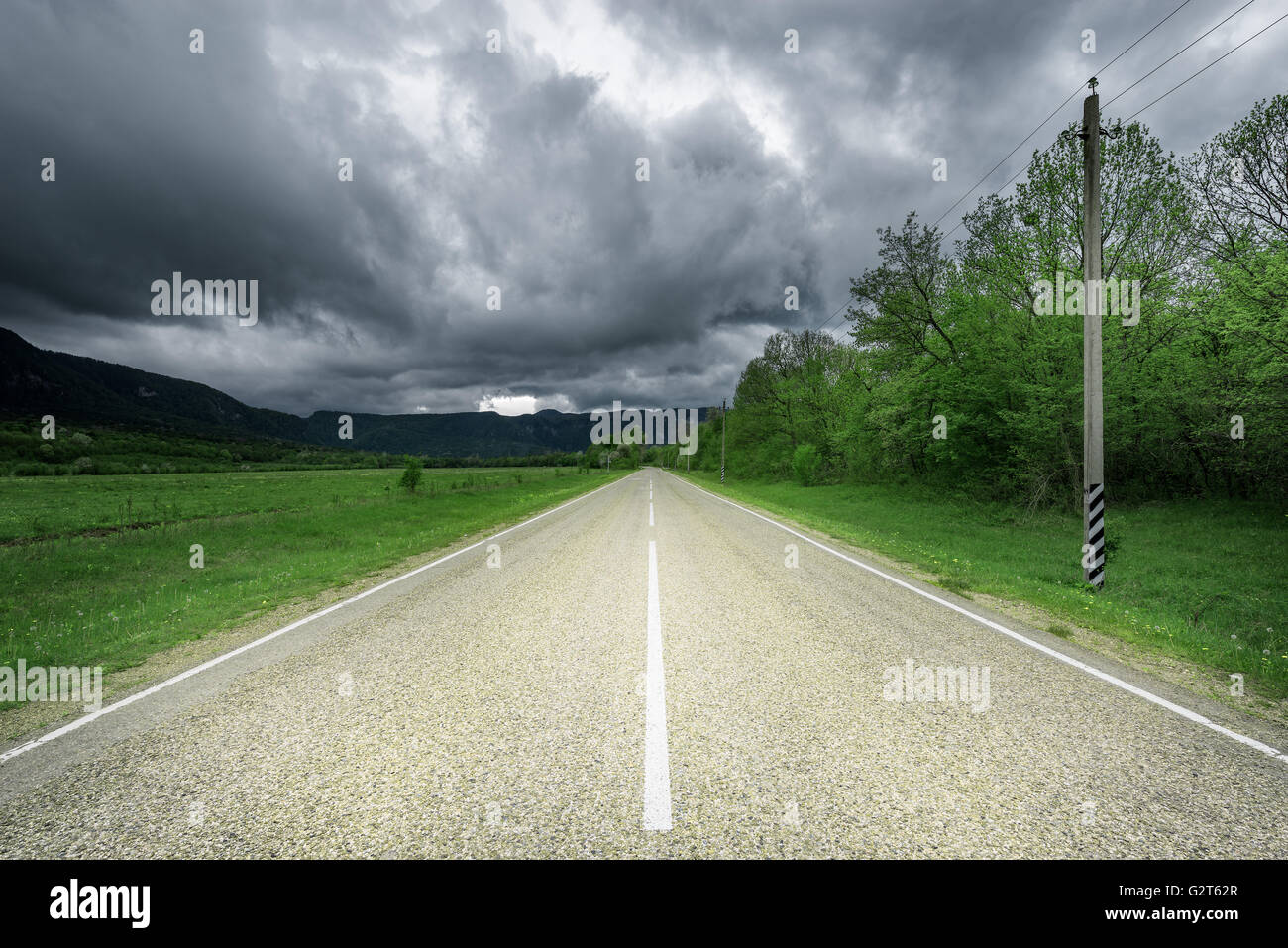 Asphalt road to the mountains under the dramatic stormy sky Stock Photo ...