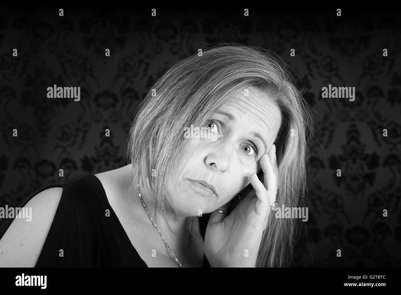 Black and white of woman looking sad on black damask Stock Photo