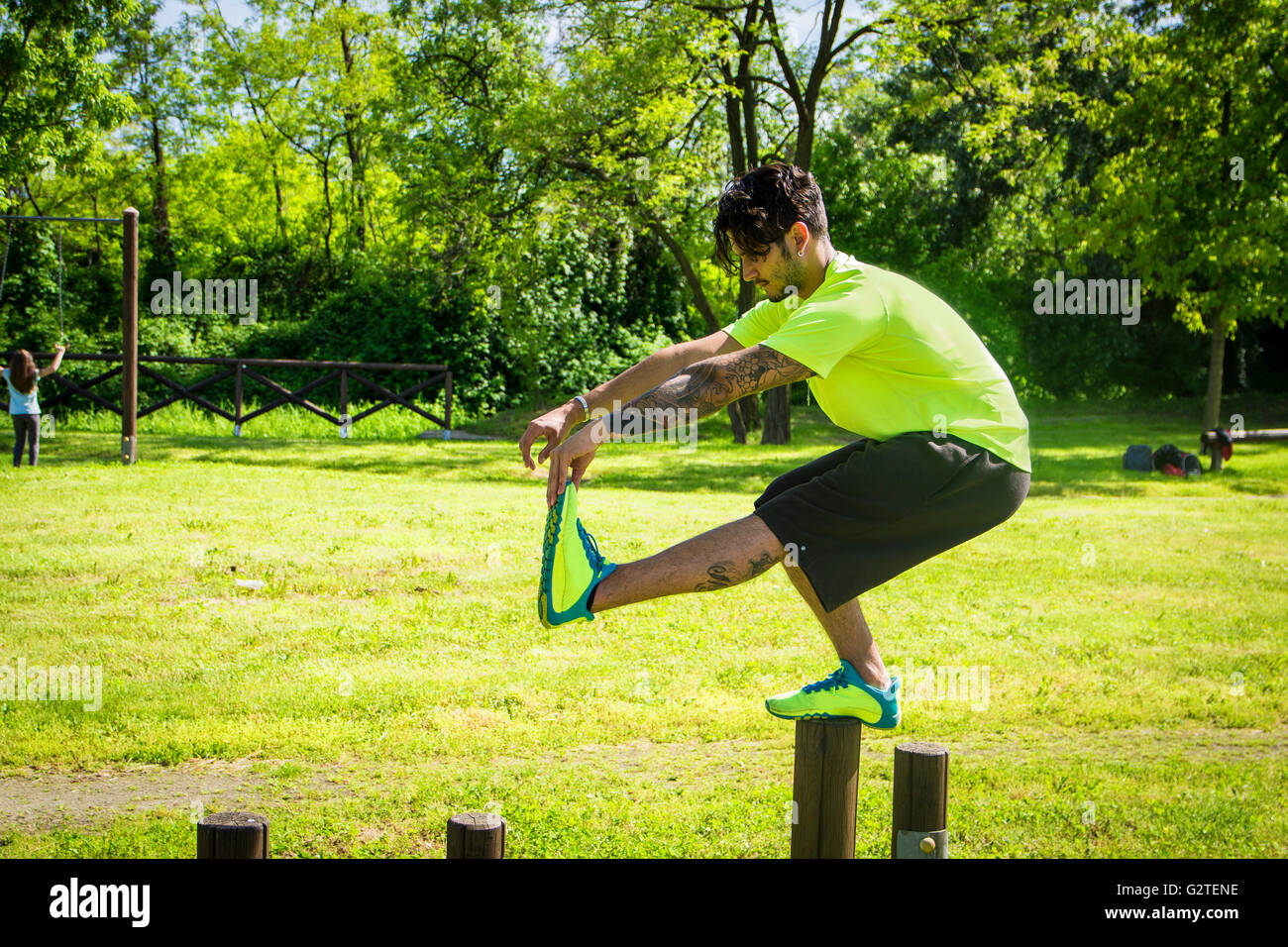 Side view of dark-haired sportsman doing pistol squats on wooden bar in park Stock Photo