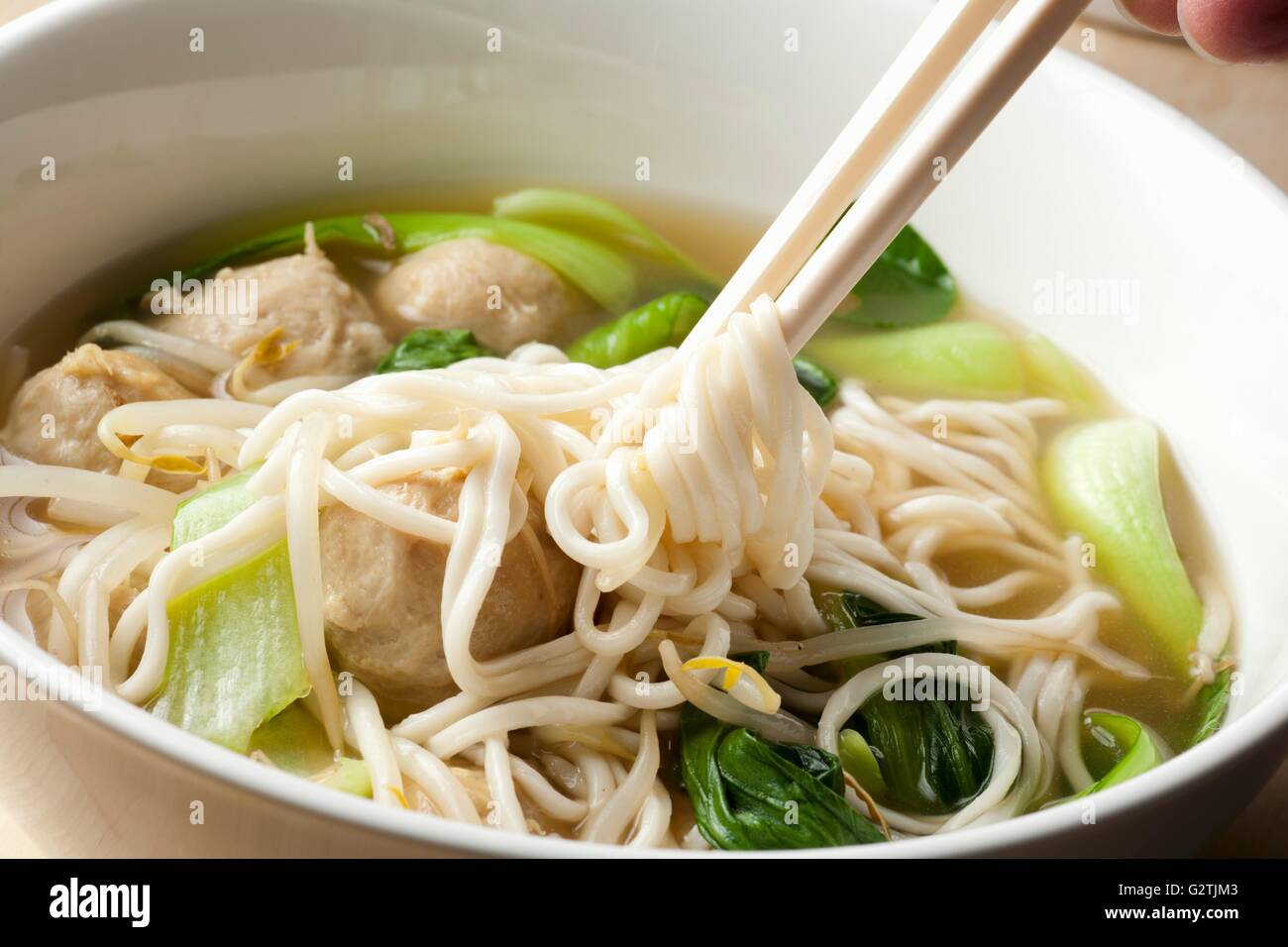 Hand Twirling Noodles from Shanghai Noodle Meatball Soup onto Chopsticks Stock Photo