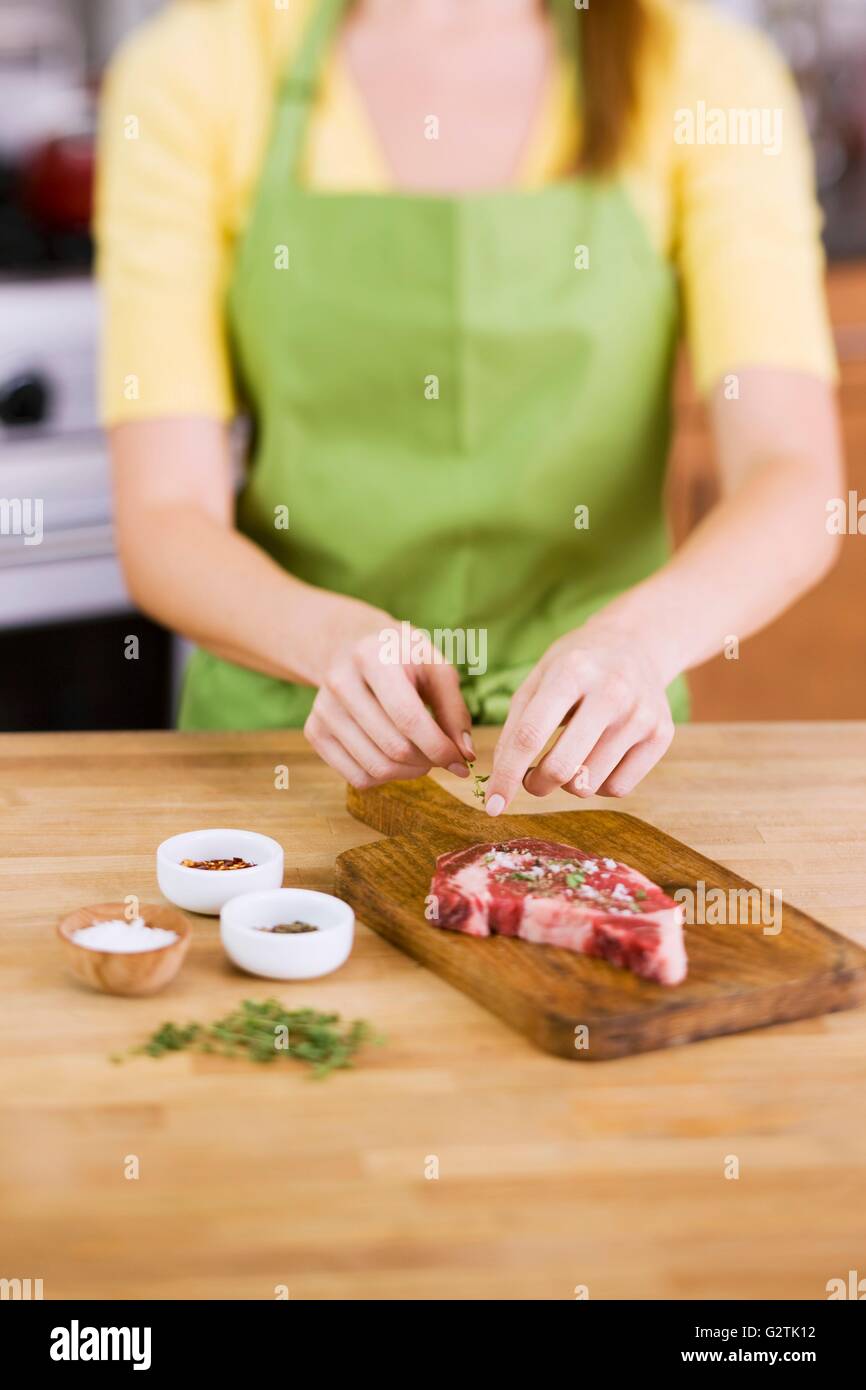 Woman Adding Fresh Herbs to Season a Steak Stock Photo