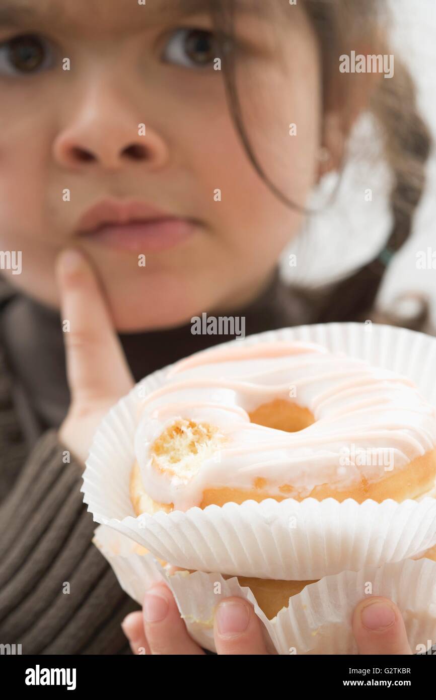 Girl with sceptical expression holding doughnut, one bite taken Stock Photo
