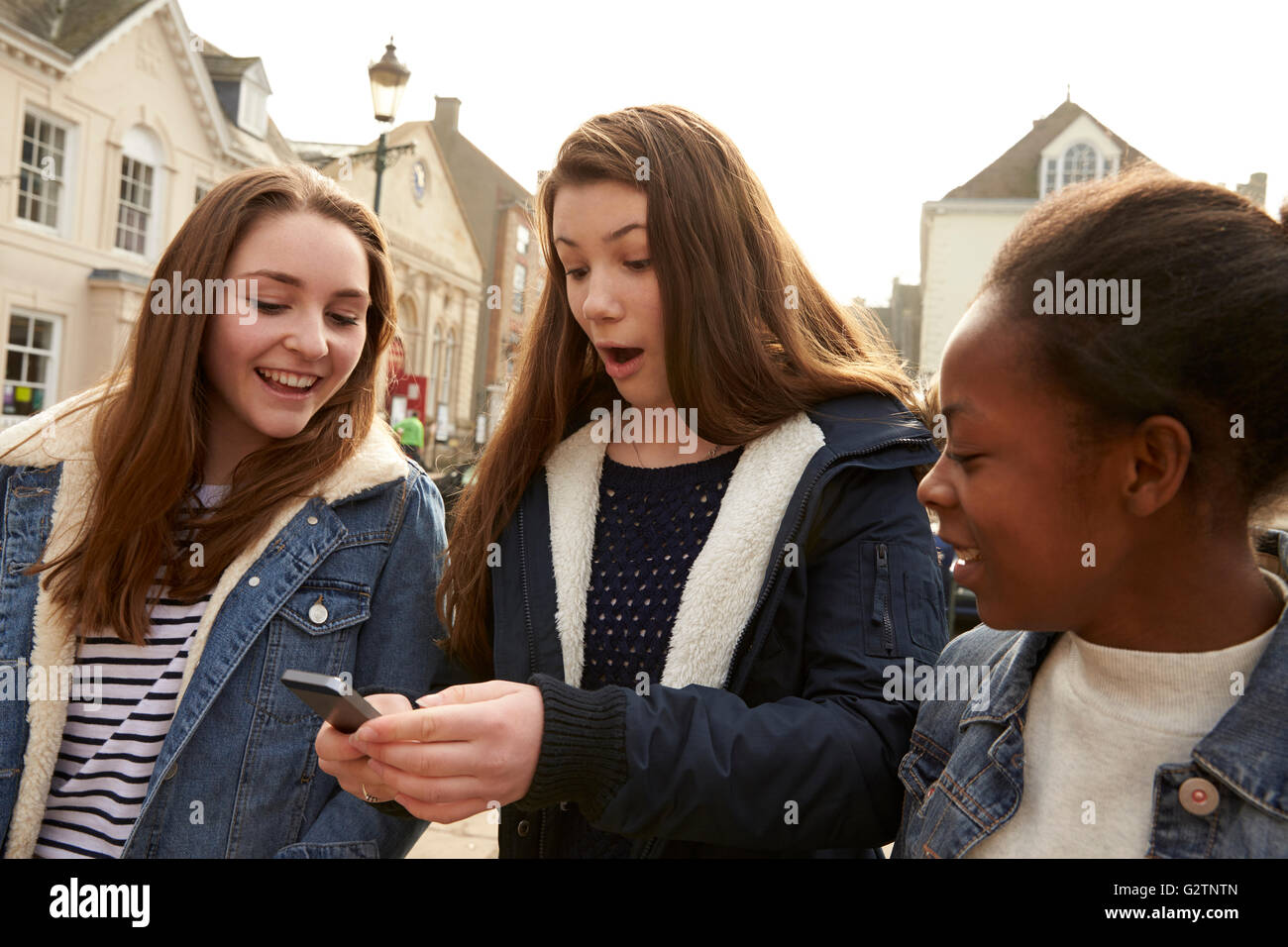 Teenage Girls Walking Along Street Looking At Social Media Stock Photo