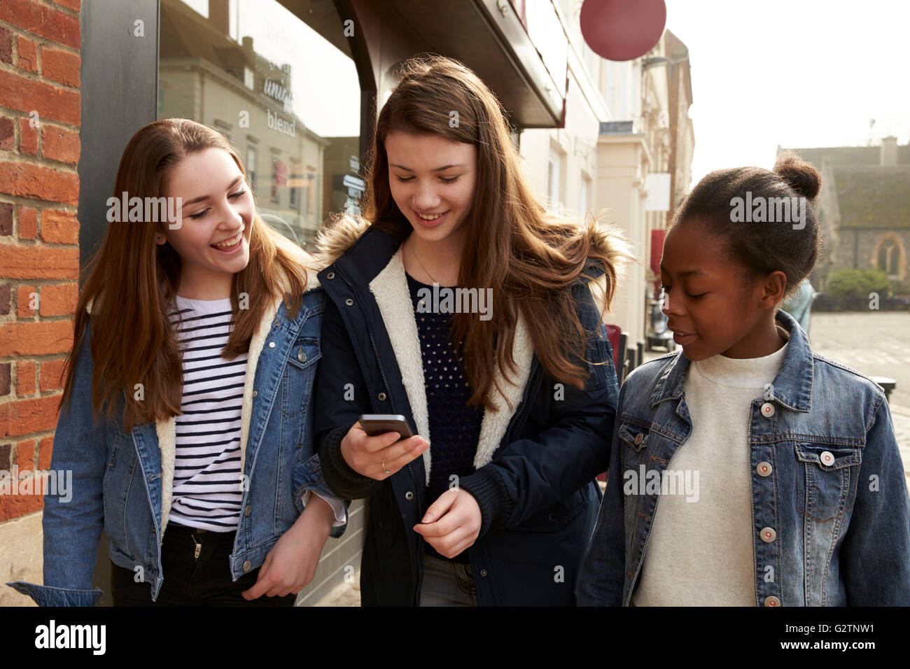 Teenage Girls Walking Along Street Looking At Social Media Stock Photo