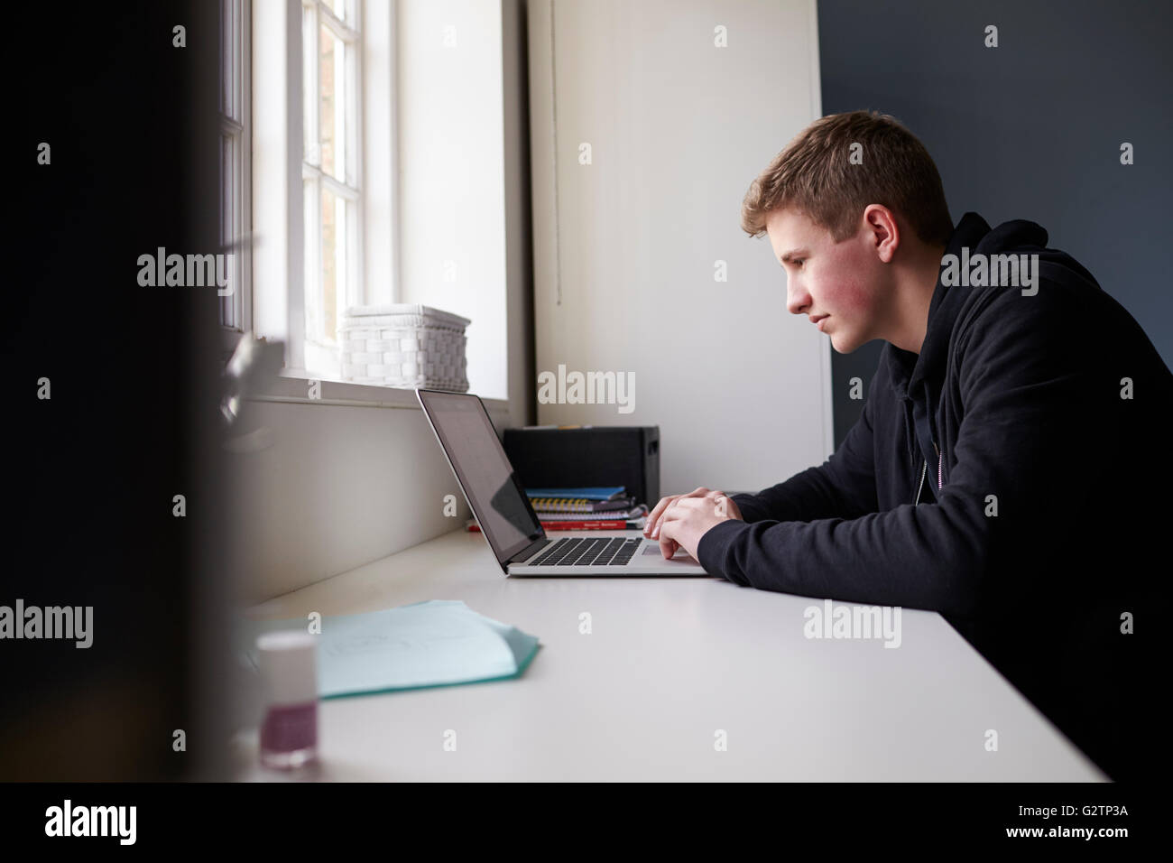 Teenage Boy Sitting At Desk In Bedroom Using Laptop Stock Photo