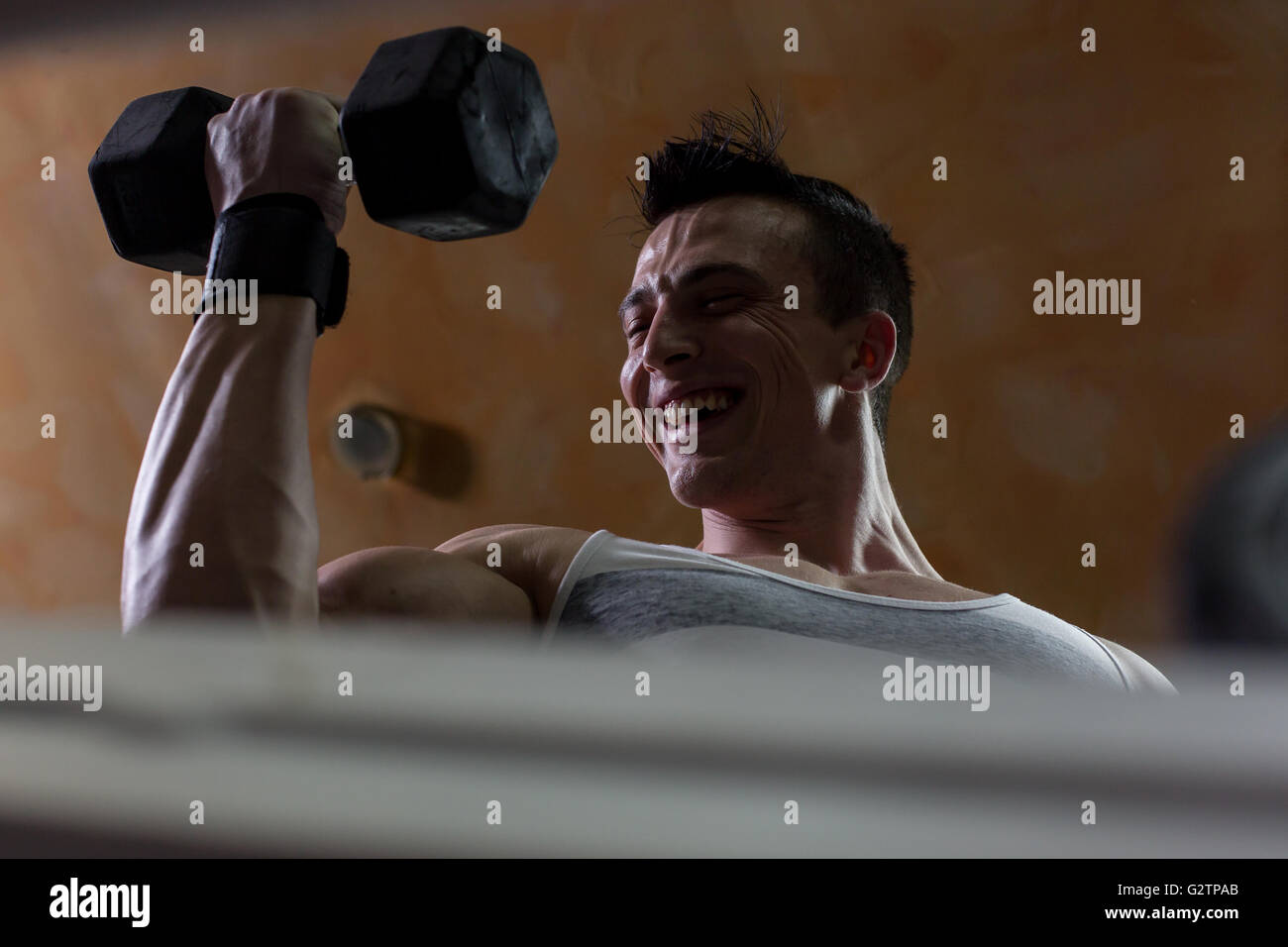 very power athletic guy bodybuilder , execute exercise with dumbbells, in dark gym Stock Photo