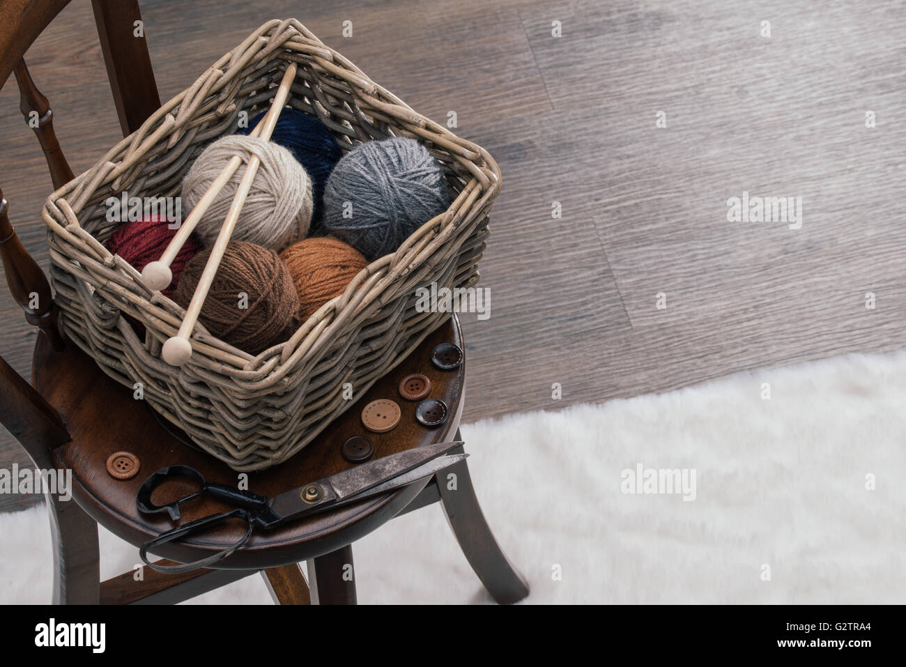 knitting needles, scissors and yarn inside old basket on wooden chair ...