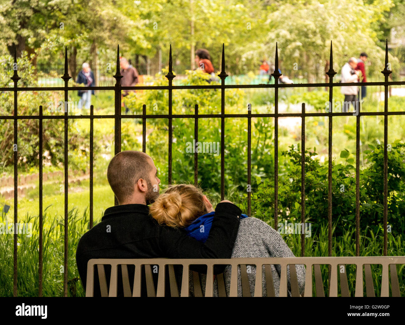 A couple on a bench hugging in front of a public garden and a railing Stock Photo