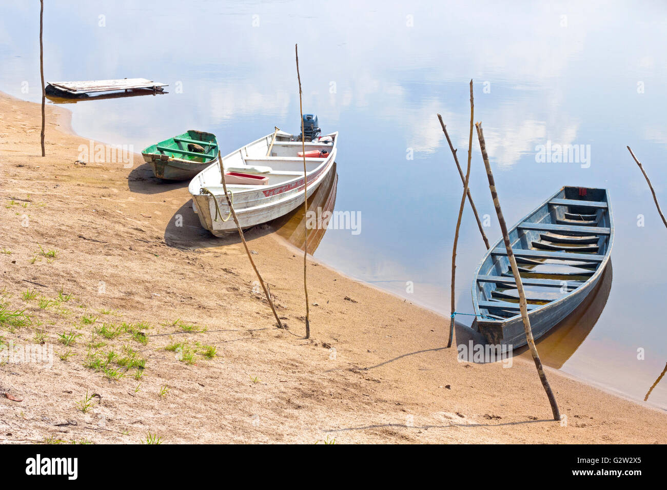Old wooden boats moored to Amazon river shore in Brazil. The sky reflects on the water. Stock Photo