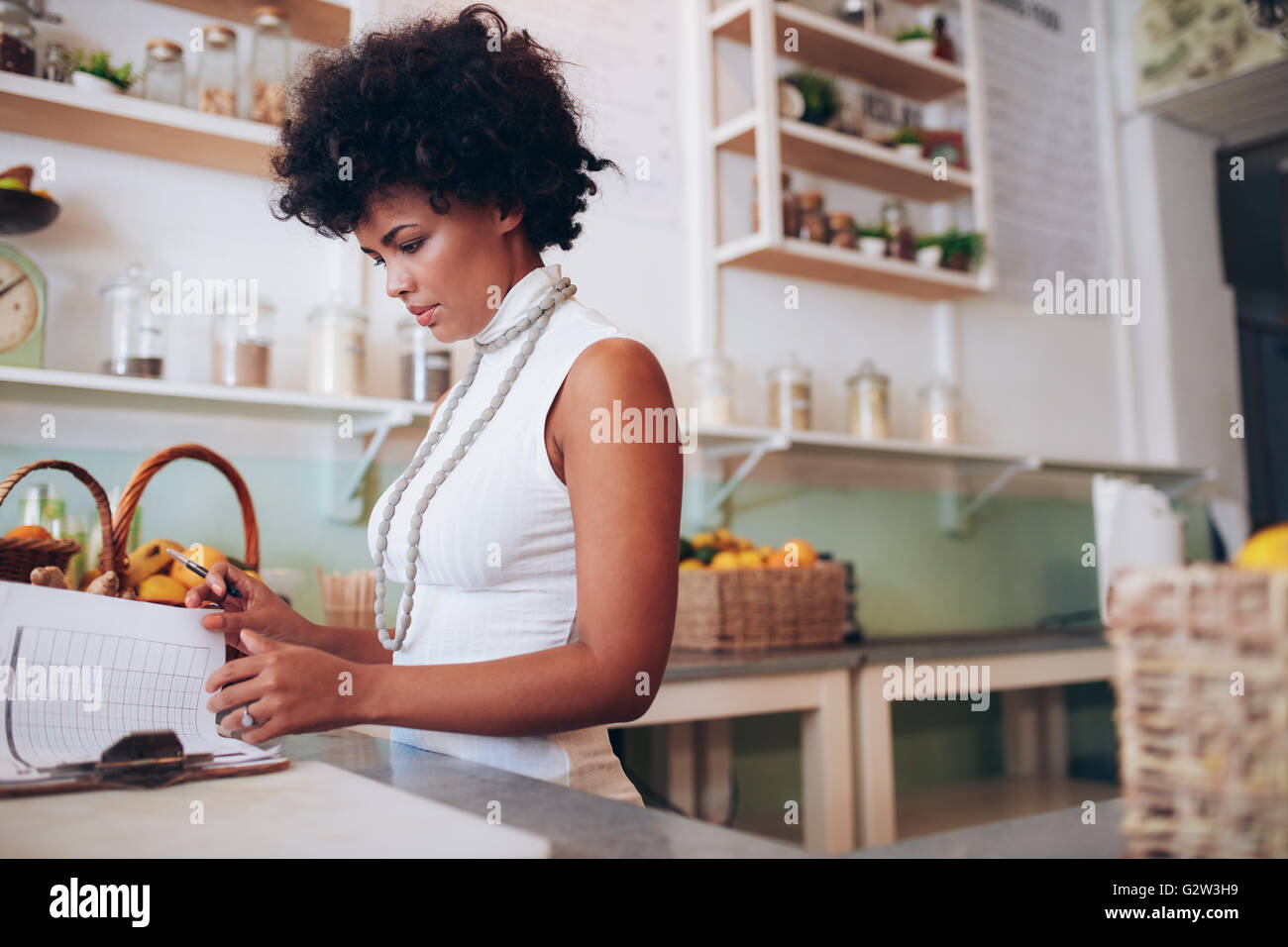 Indoor shot of young african woman doing accounts. Female juice bar owner standing behind the counter and looking at some papers Stock Photo