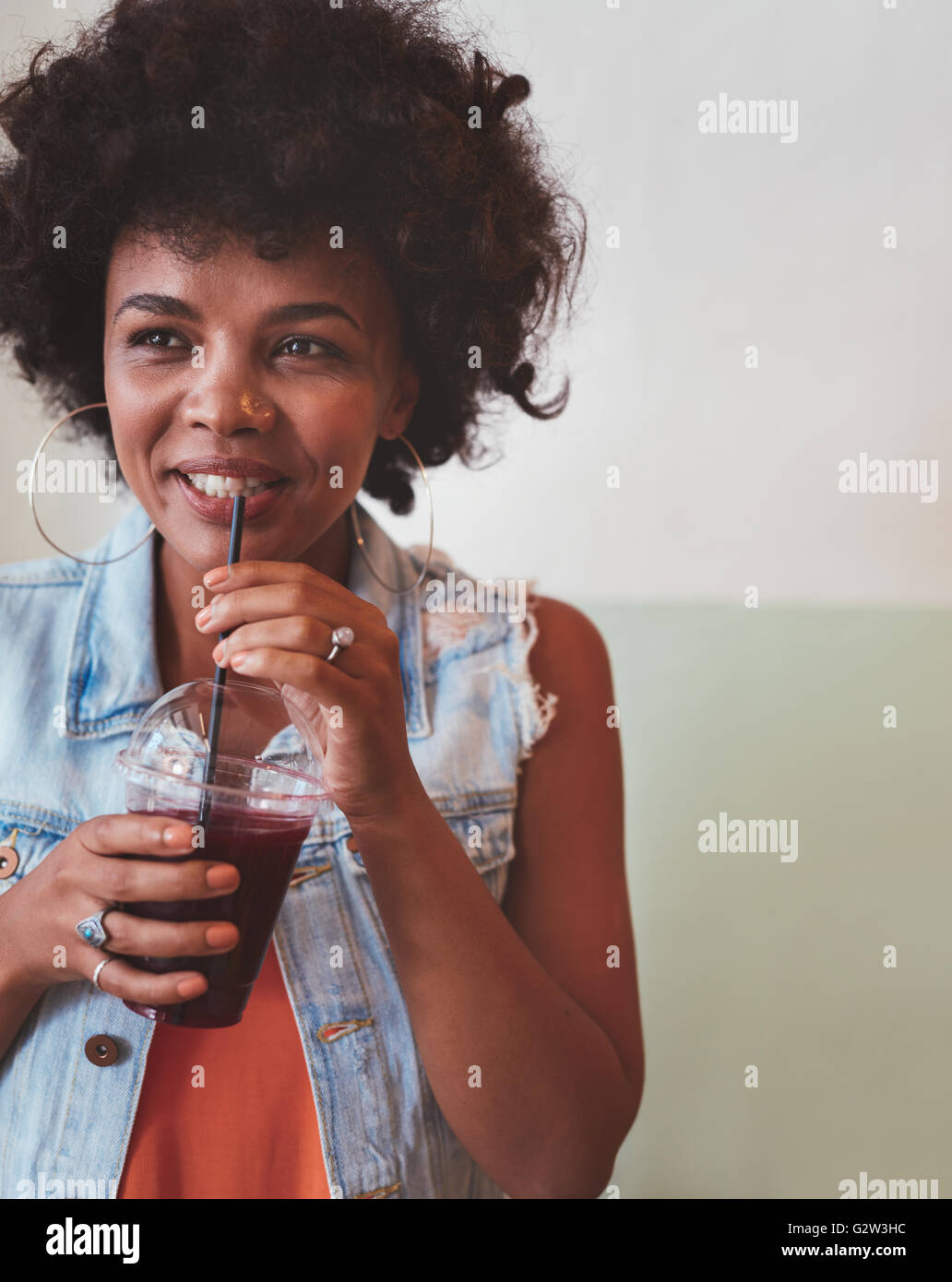 Close up image of young african woman drinking fresh fruit juice and looking away. Stock Photo