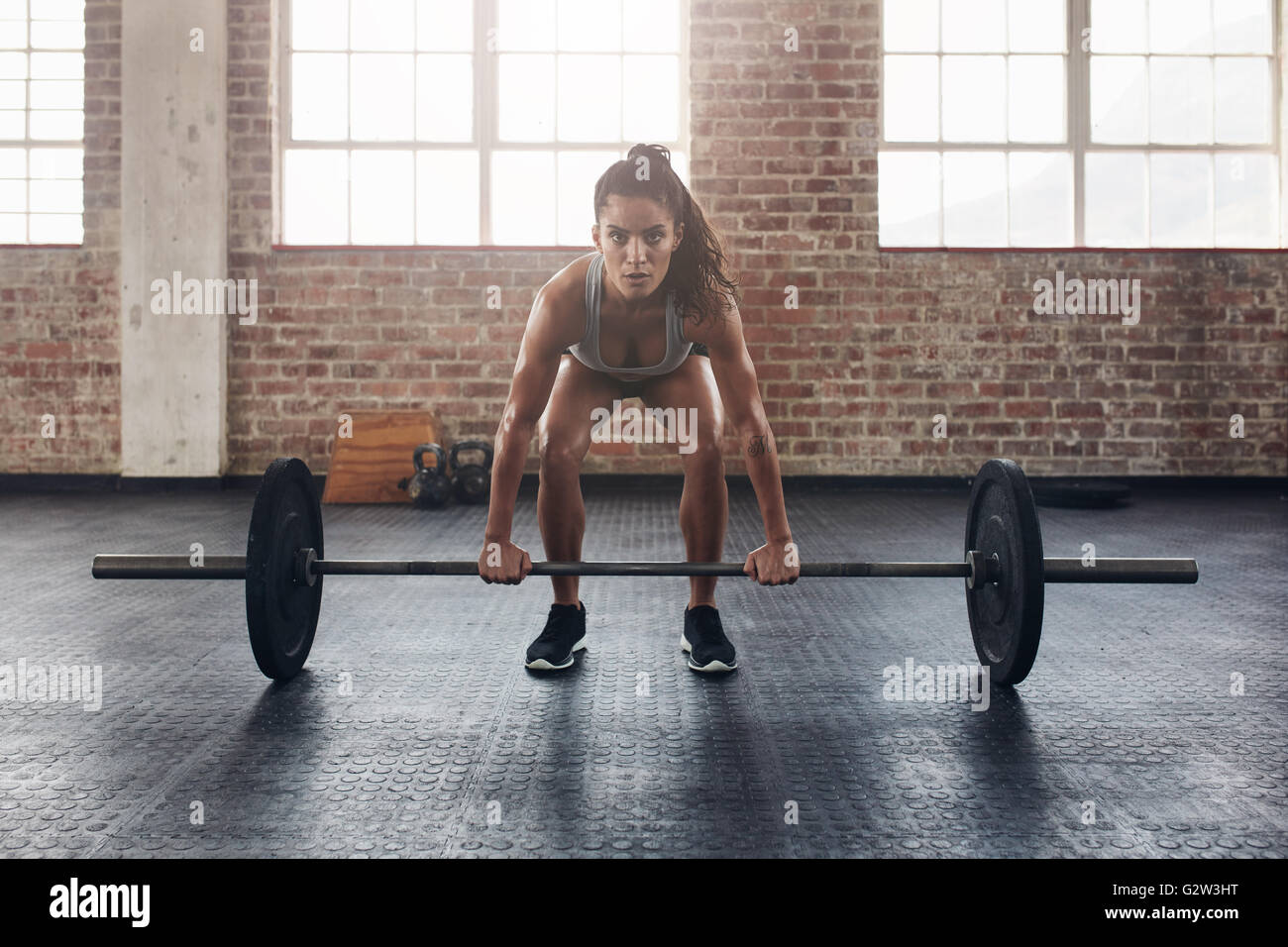Female performing deadlift exercise with weight bar. Confident young woman doing weight lifting workout at gym. Stock Photo