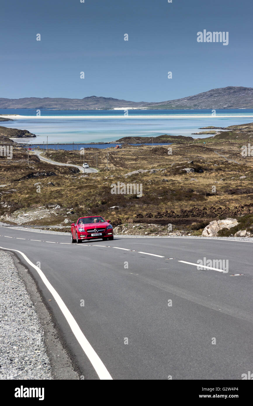 Red car traveling towards Tarbert Isle of Harris with Luskentyre beach in the background Isle of Harris Western Isles . Stock Photo