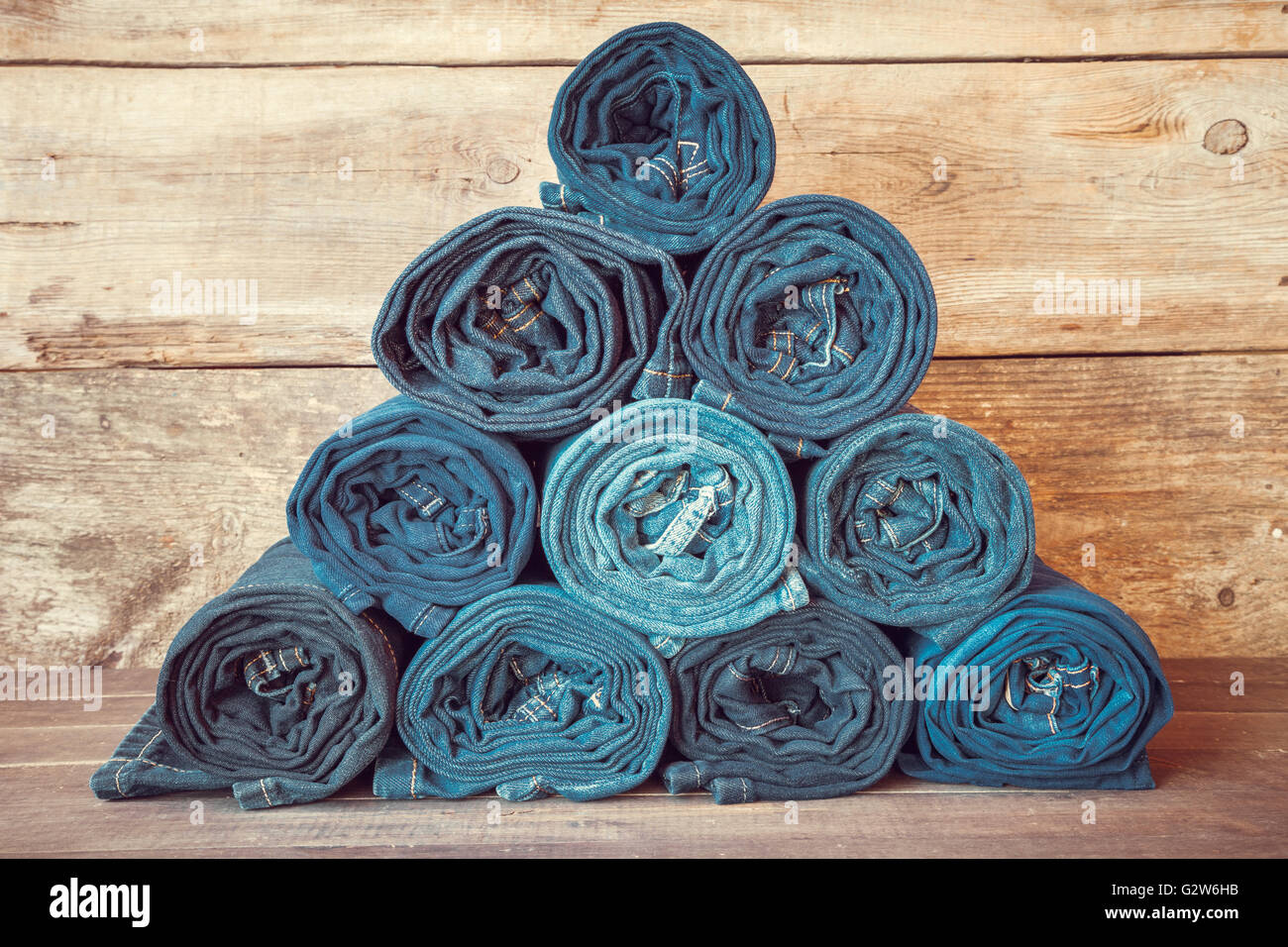 Rolled jeans stack on wooden background, retro toned. Stock Photo