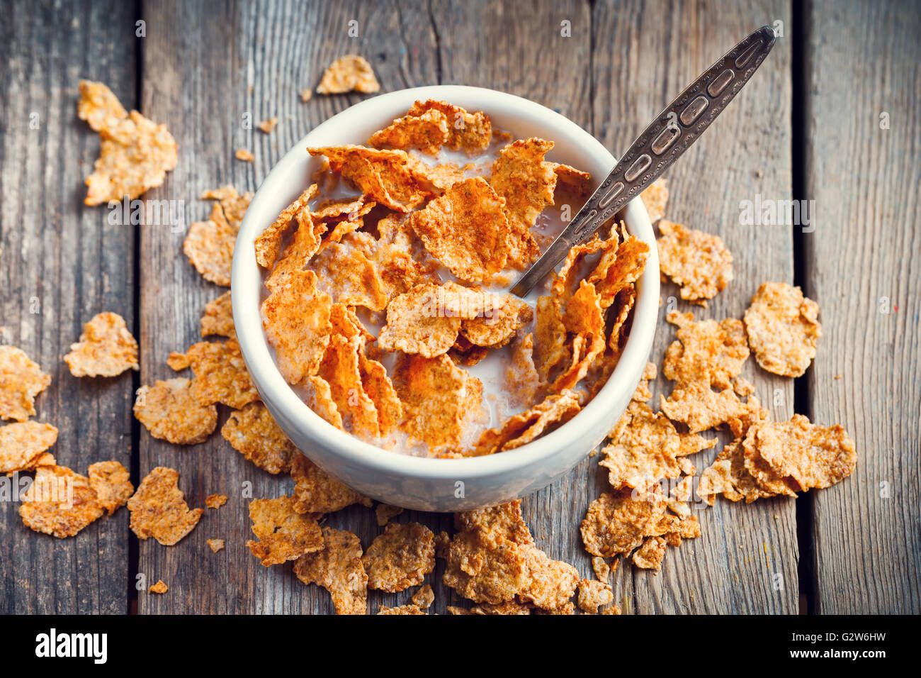 Breakfast cereal wheat flakes in bowl with milk on wooden table Stock Photo