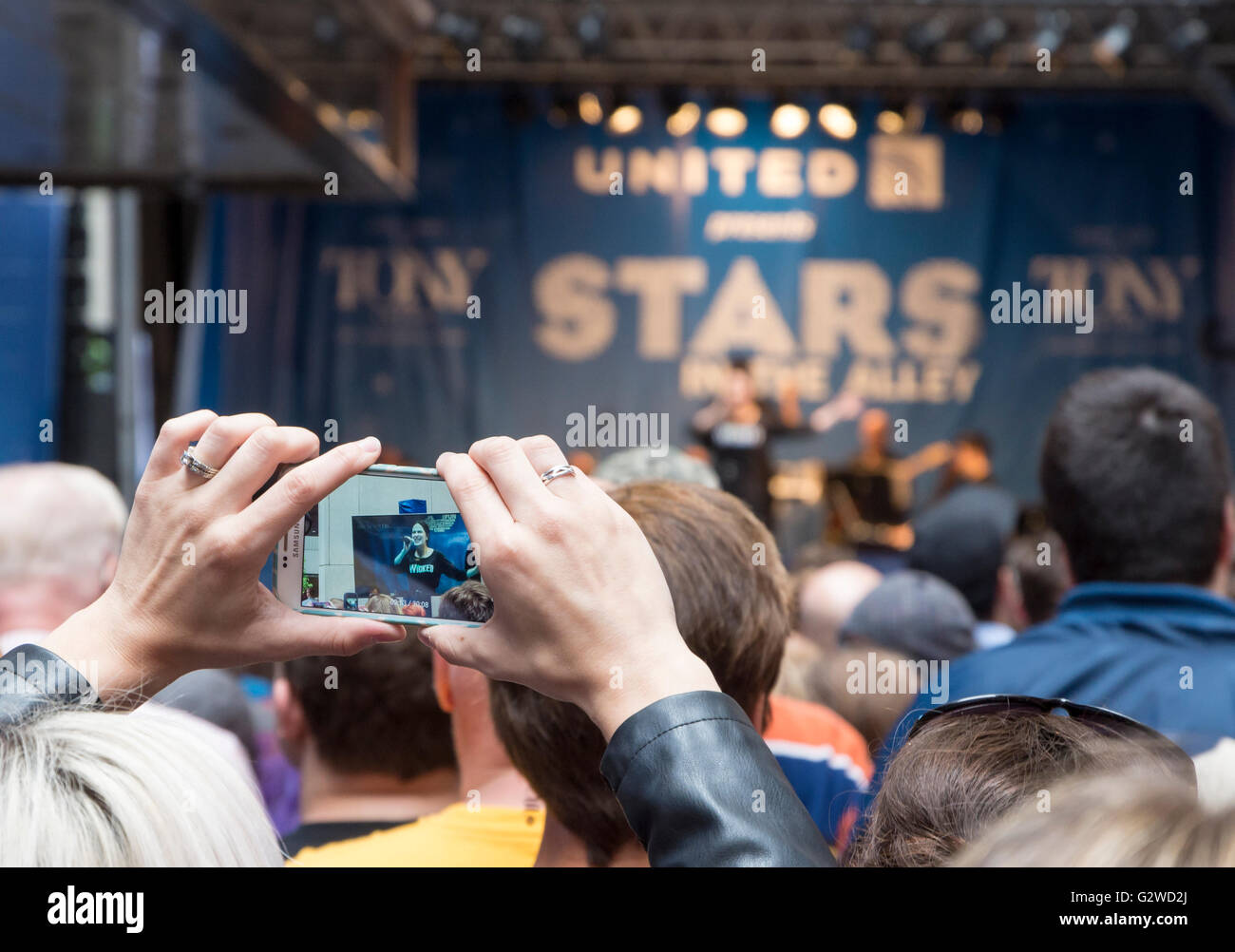 Woman recording a performance of a song from the musical Wicked on her mobile phone at the free Stars in the Alley concert on Broadway, New York. Shallow depth of field with focus on the phone screen. Stock Photo
