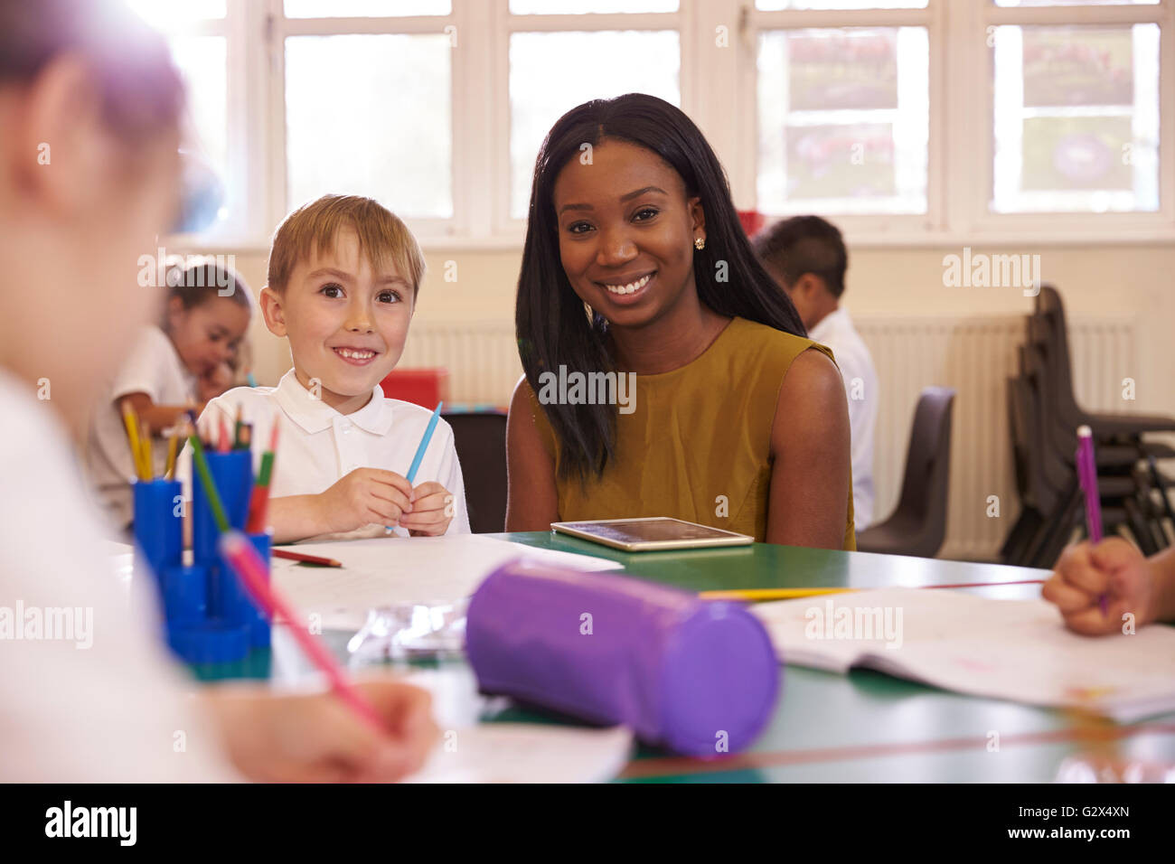 Elementary School Teacher Helping Male Pupil At Desk Stock Photo - Alamy