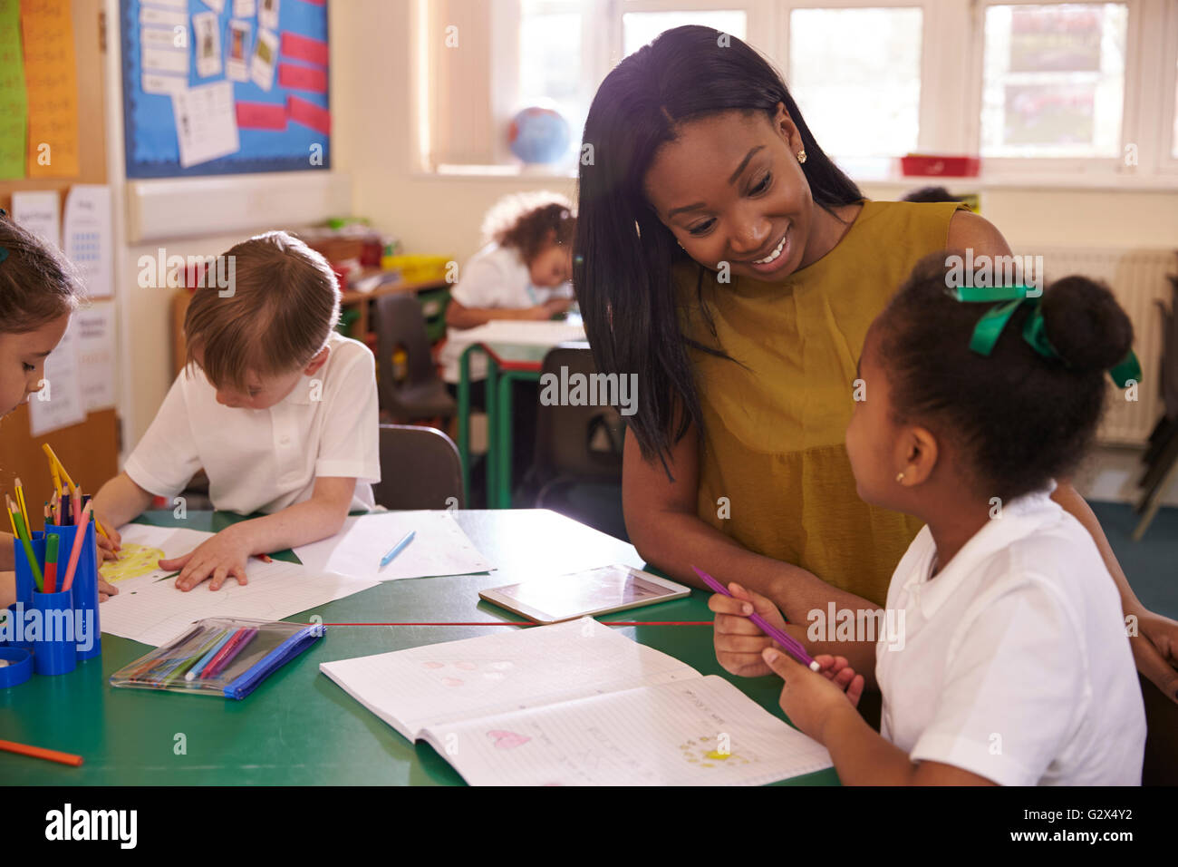 Elementary School Teacher Helping Female Pupil At Desk Stock Photo