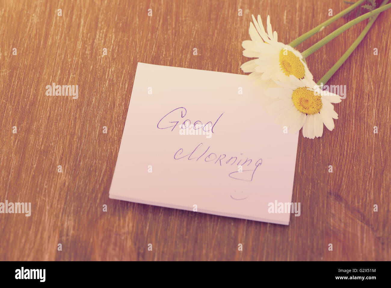 Daisy flower and piece of paper with text 'good morning' on the wooden table. Photo in vintage style Stock Photo