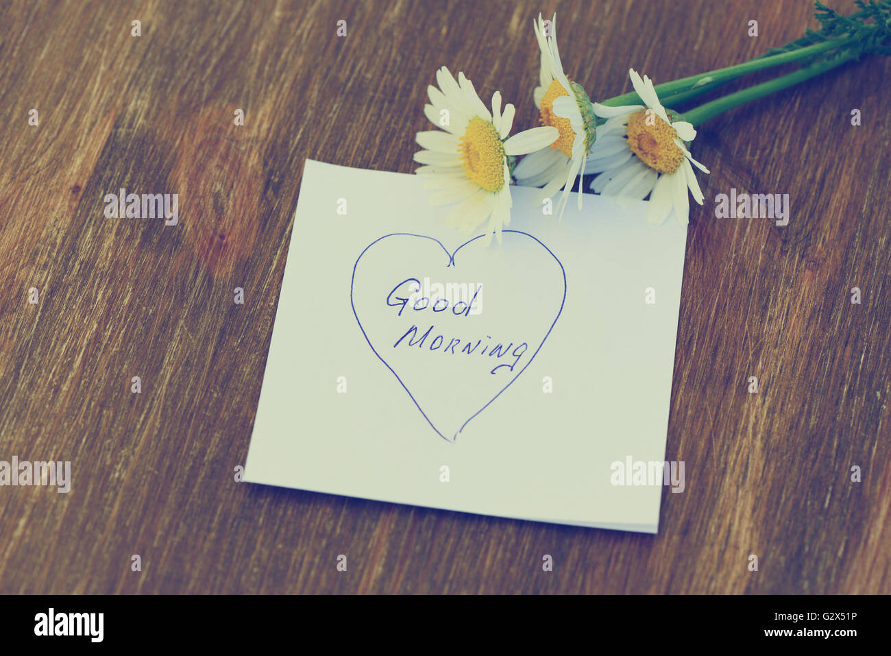 Daisy flower and piece of paper with text 'good morning' on the wooden table. Photo in vintage style Stock Photo
