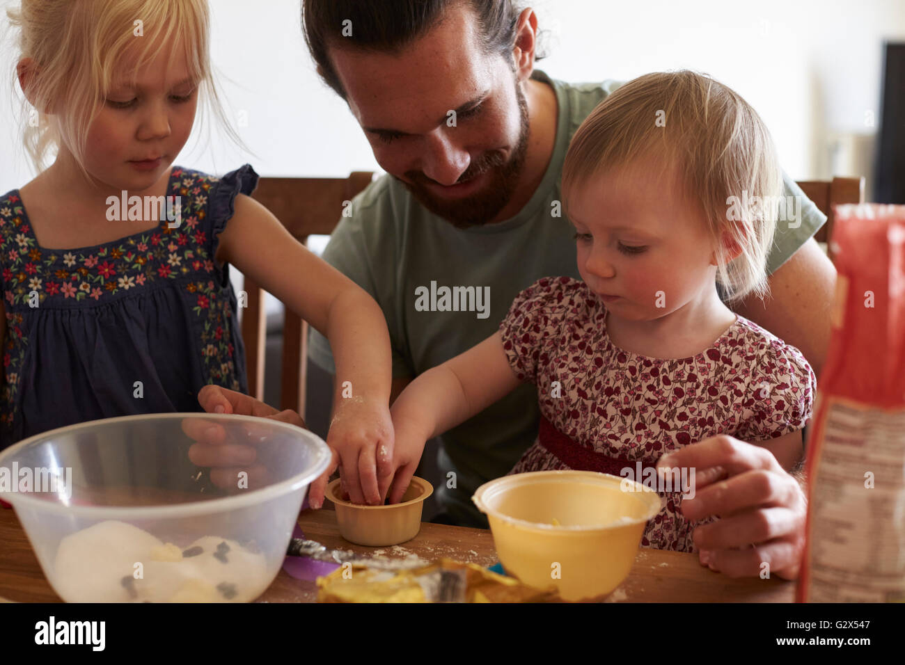 Father With Daughters At Home Baking Cakes Together Stock Photo