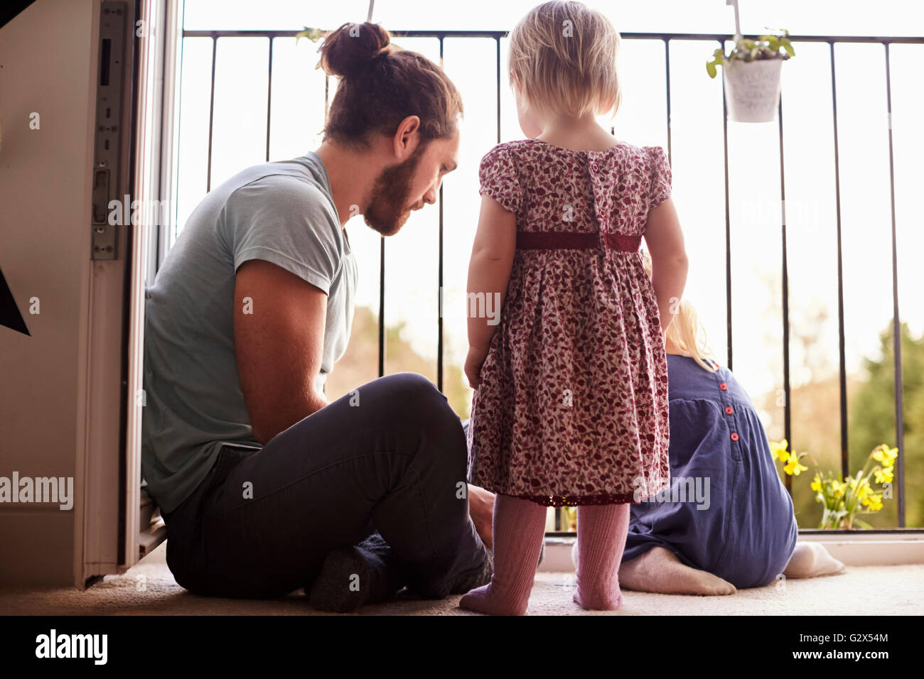 Father With Children At Home Watering Plants On Balcony Stock Photo