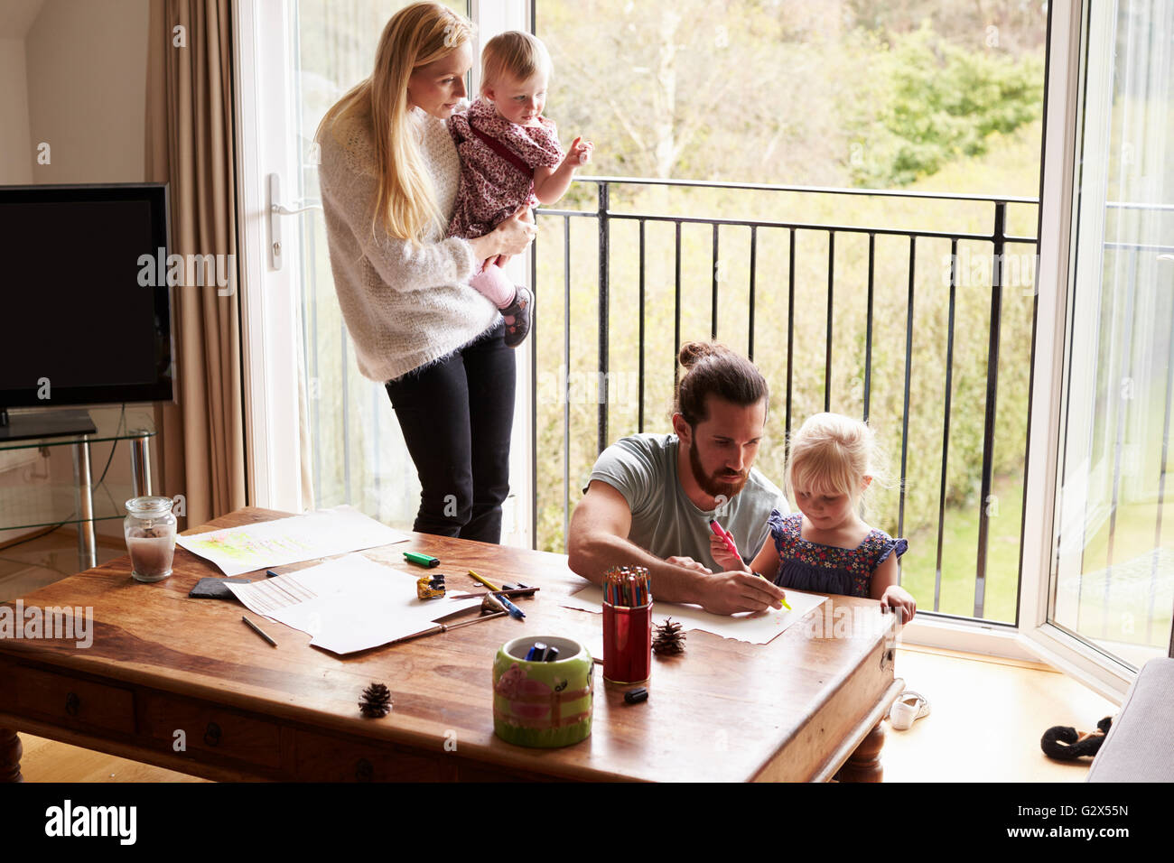 Family Sitting At Table And Drawing Pictures Together Stock Photo