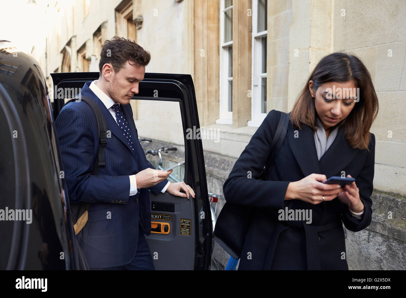 Businesspeople Getting Out Of Taxi Using Mobile Phones Stock Photo