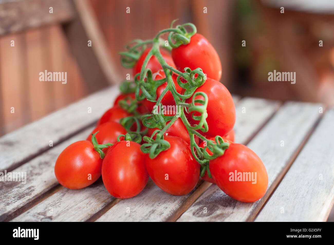 Branch of red ripe cherry tomatoes on wooden table, selective focus Stock Photo