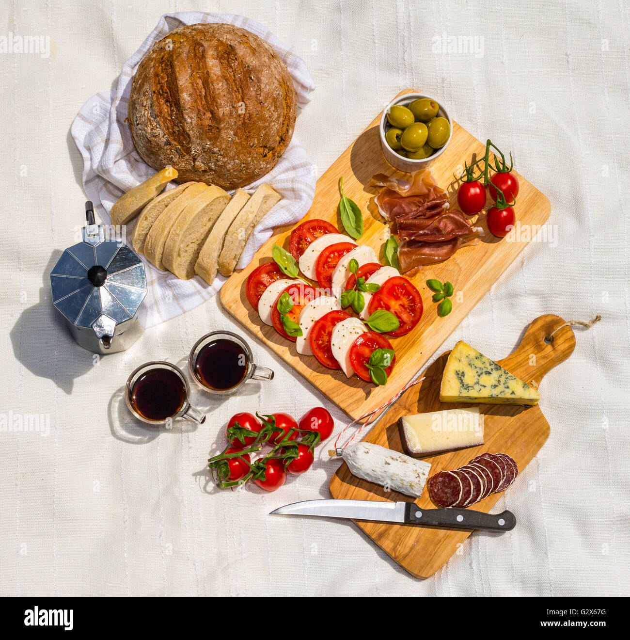 Aerial view of an outdoor picnic consisting of rustic bread, ciabatta, espresso in cups, olives, tomatoes, parma ham, mozzarella Stock Photo