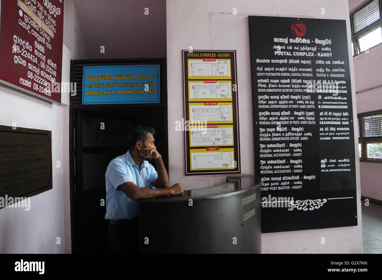A staff is standing in front of the sign 'Productivity Promotion Unit' at the entrance of Kandy Postal Office, Sri Lanka Stock Photo