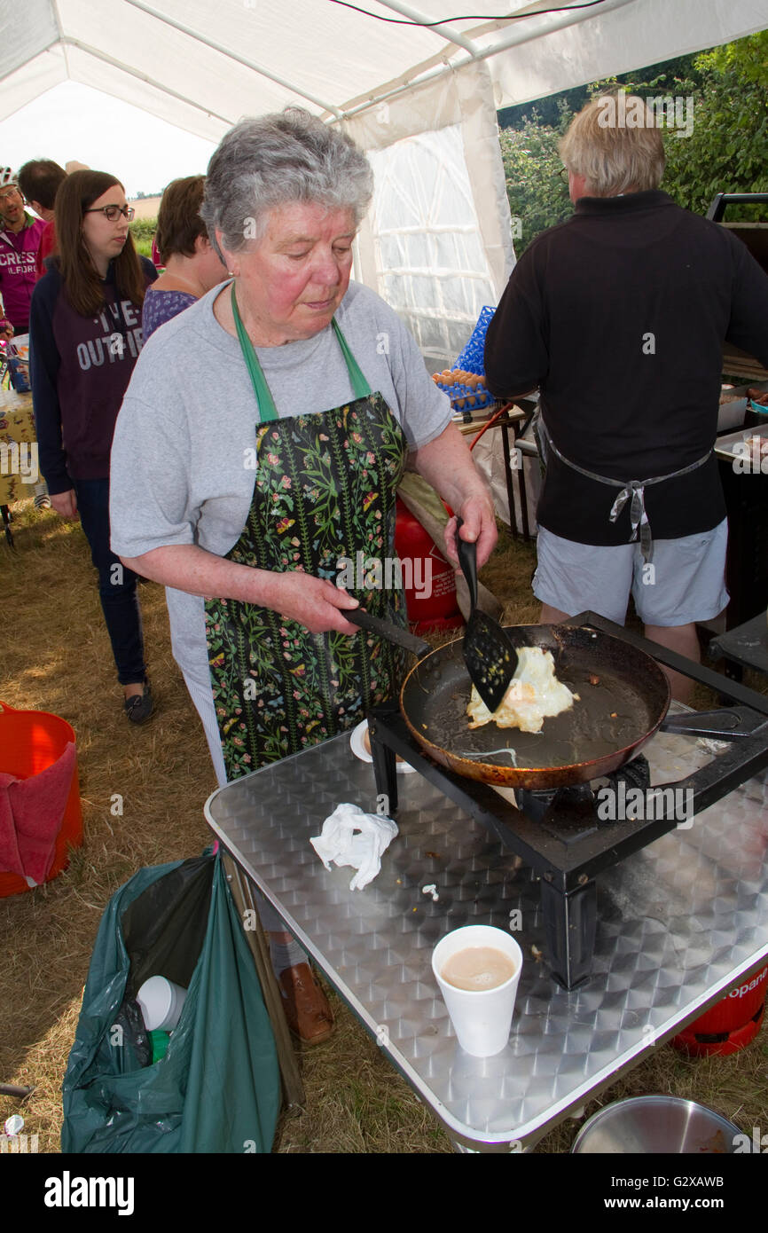 An older woman frying an egg at a pop up cafe on the Dunwich Dynamo bicycle ride Stock Photo